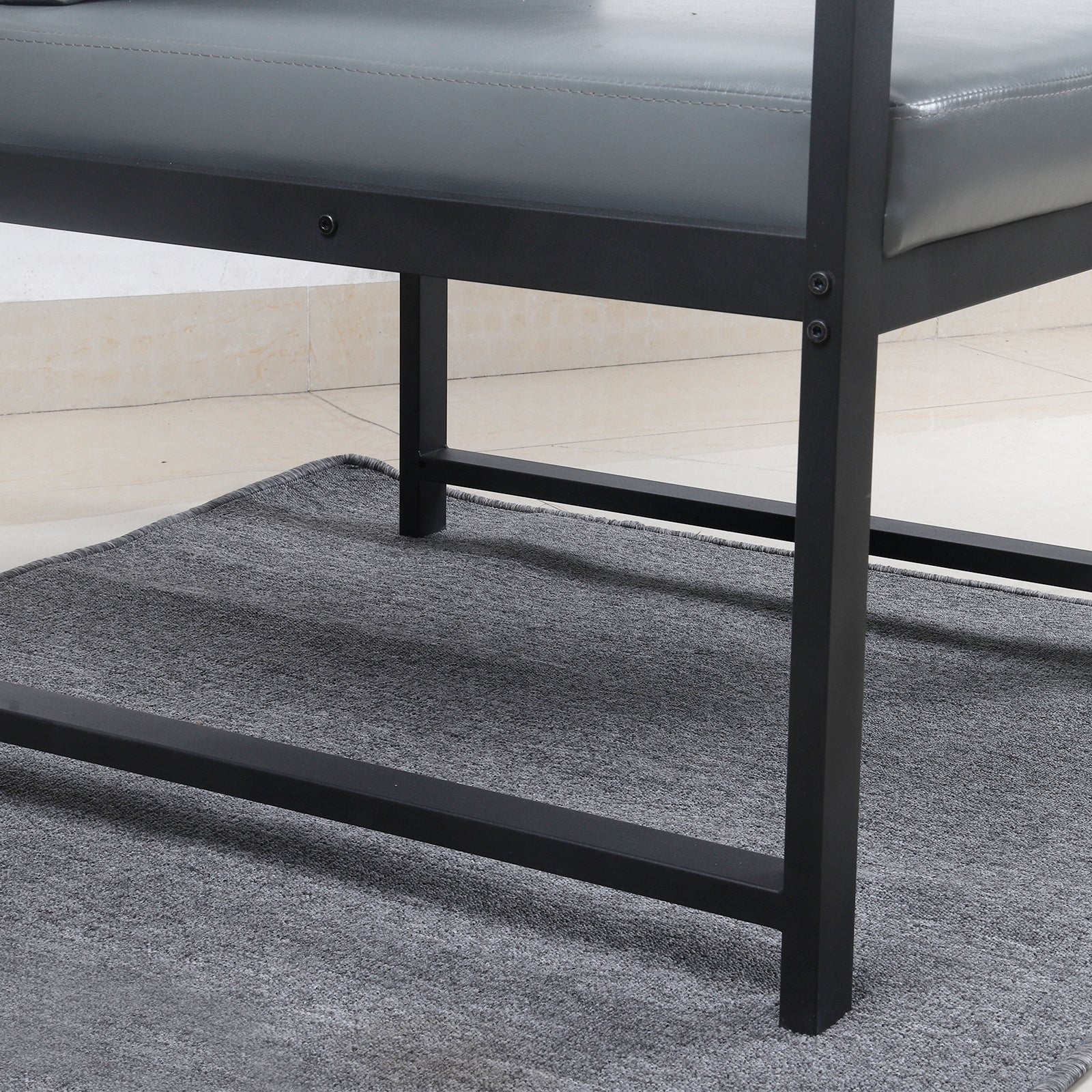 Closeup of gray faux leather bench seat with black metal frame legs on a textured rug