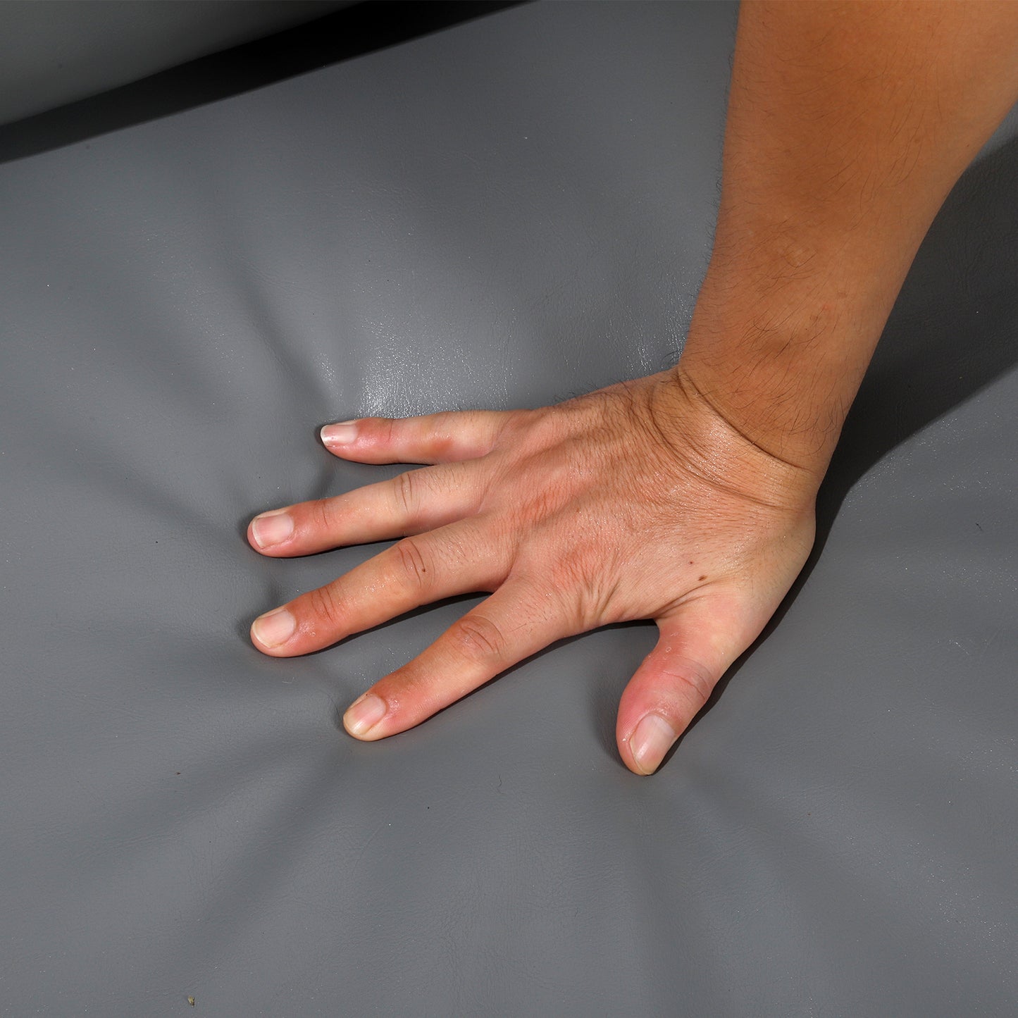 Closeup of a hand pressing into soft grey faux leather upholstery