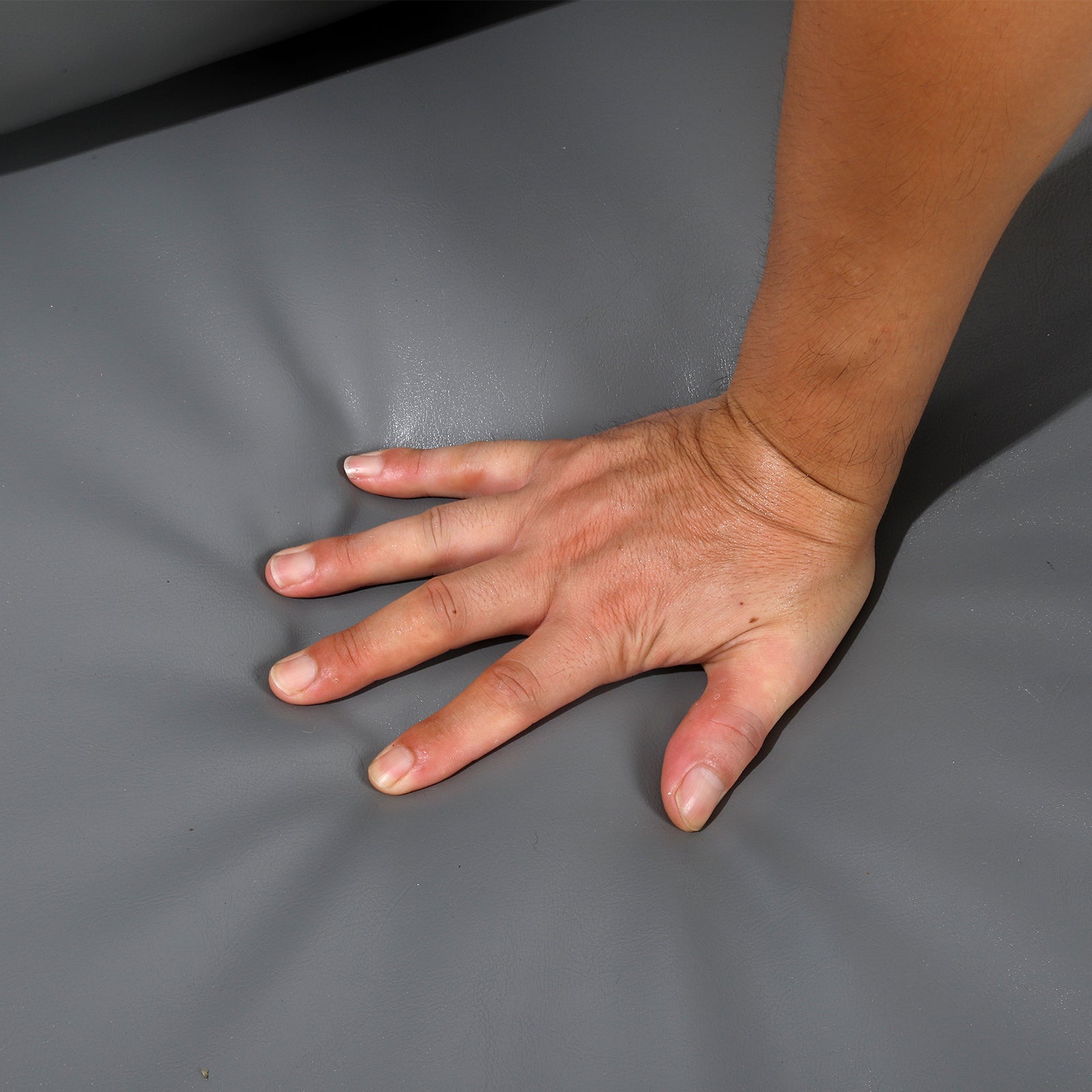 Closeup of a hand pressing into soft grey faux leather upholstery
