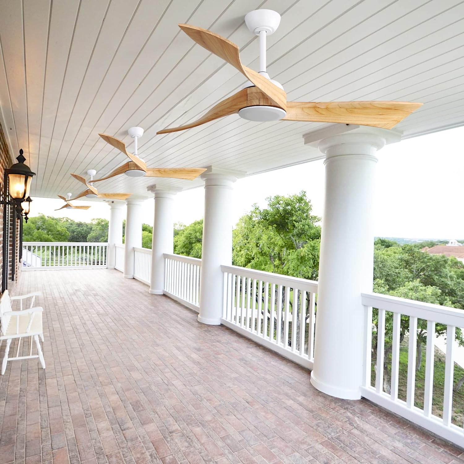 Four modern outdoor ceiling fans with natural wood blades mounted on a covered porch