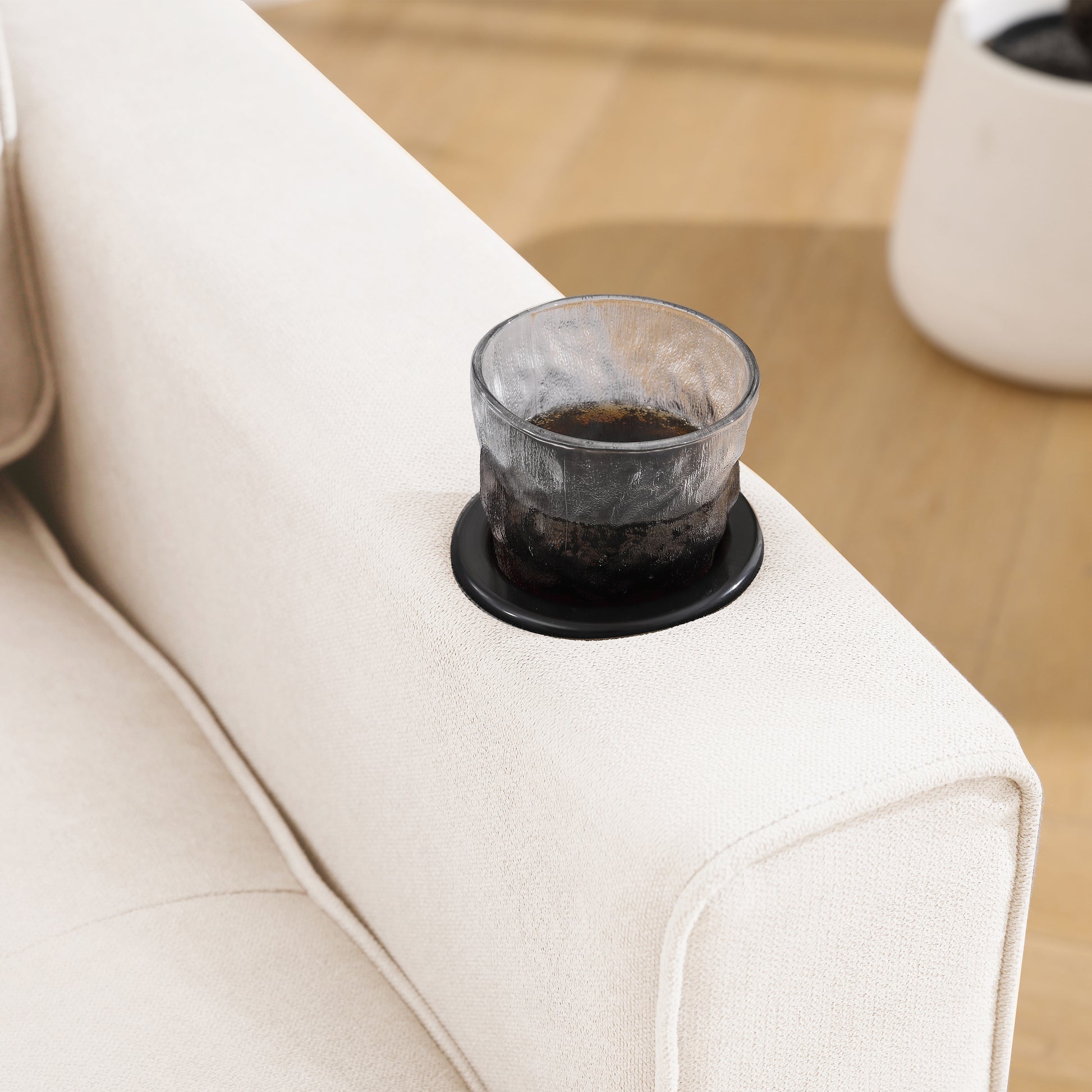Cream fabric recliner armrest with builtin cup holder and a glass of dark beverage