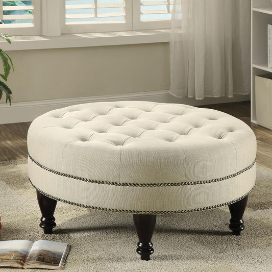 Tufted round ottoman with beige linen upholstery and decorative nailhead trim