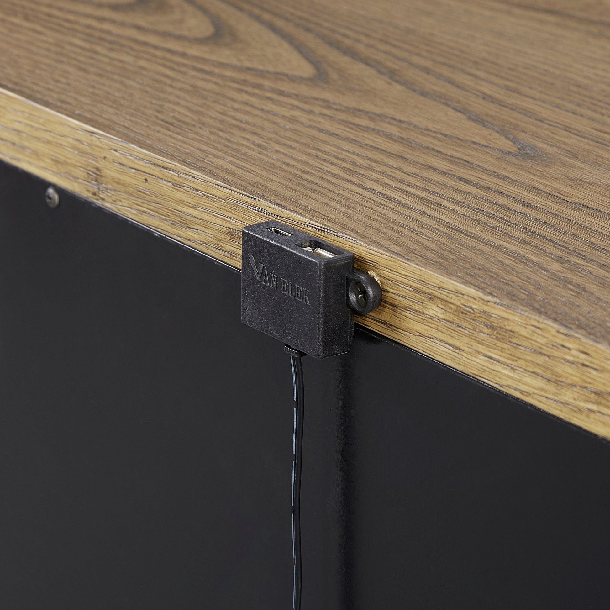 Black integrated USB charging port on a faux wood desk edge with metal trim