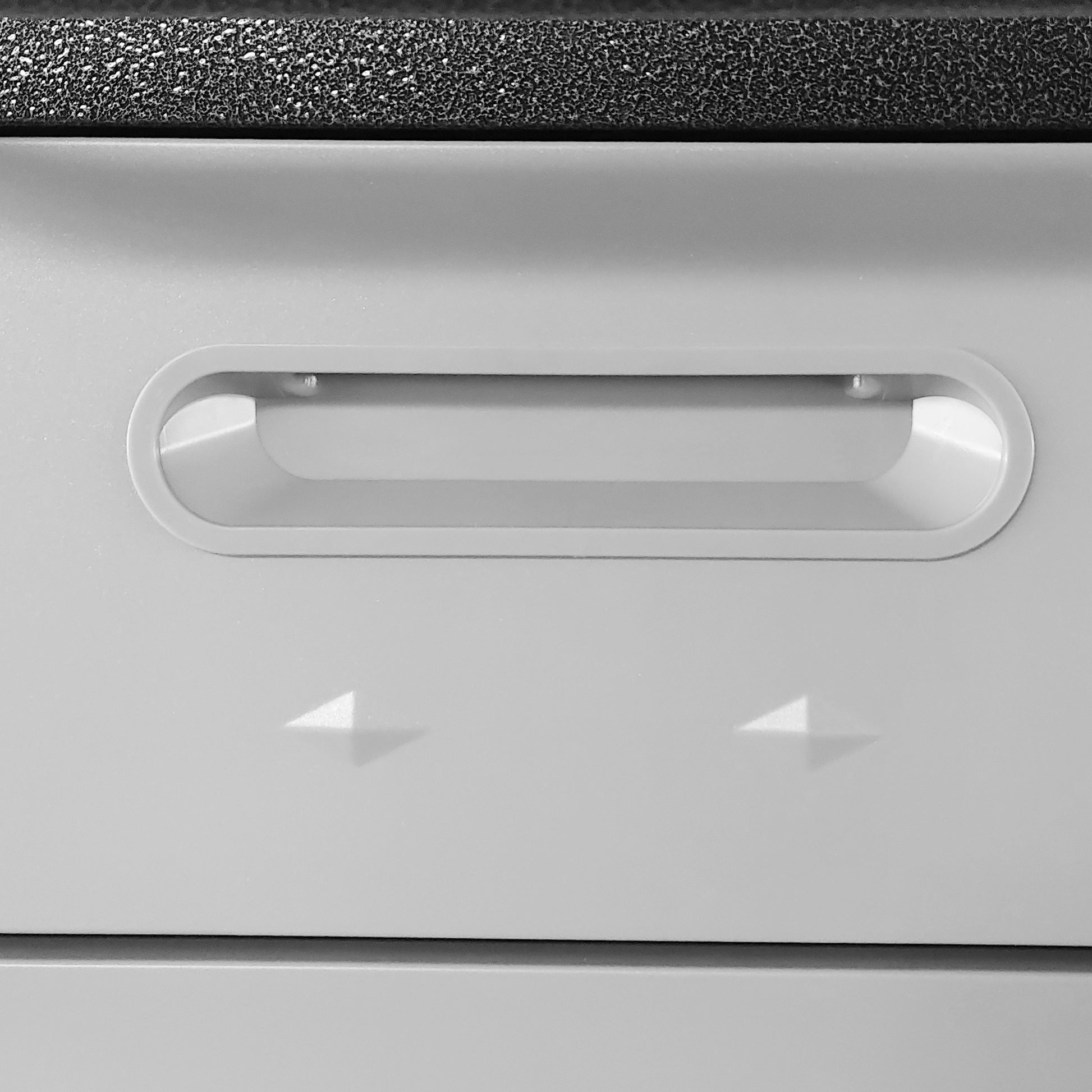 Closeup of a recessed gray plastic drawer pull with a textured black top edge