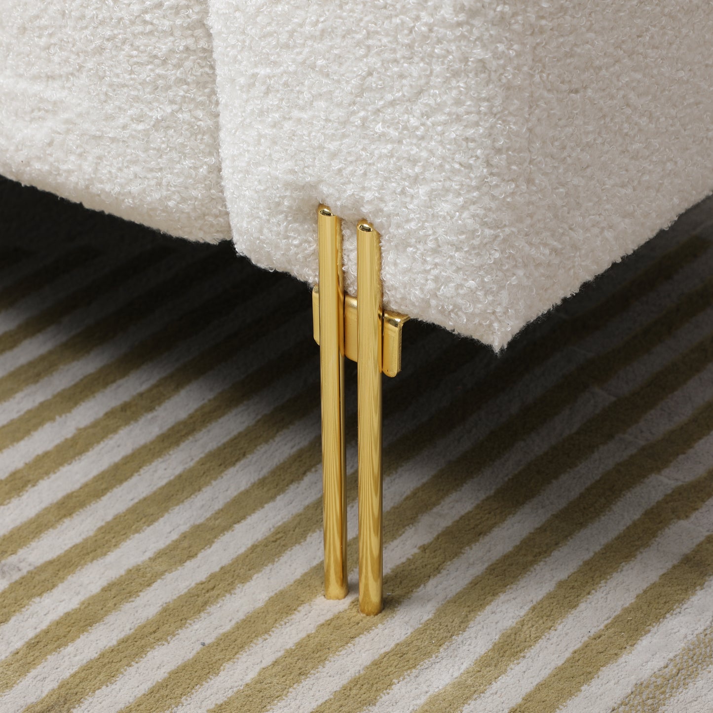 Closeup of plush white boucle fabric sofa leg with polished gold accents modern furniture