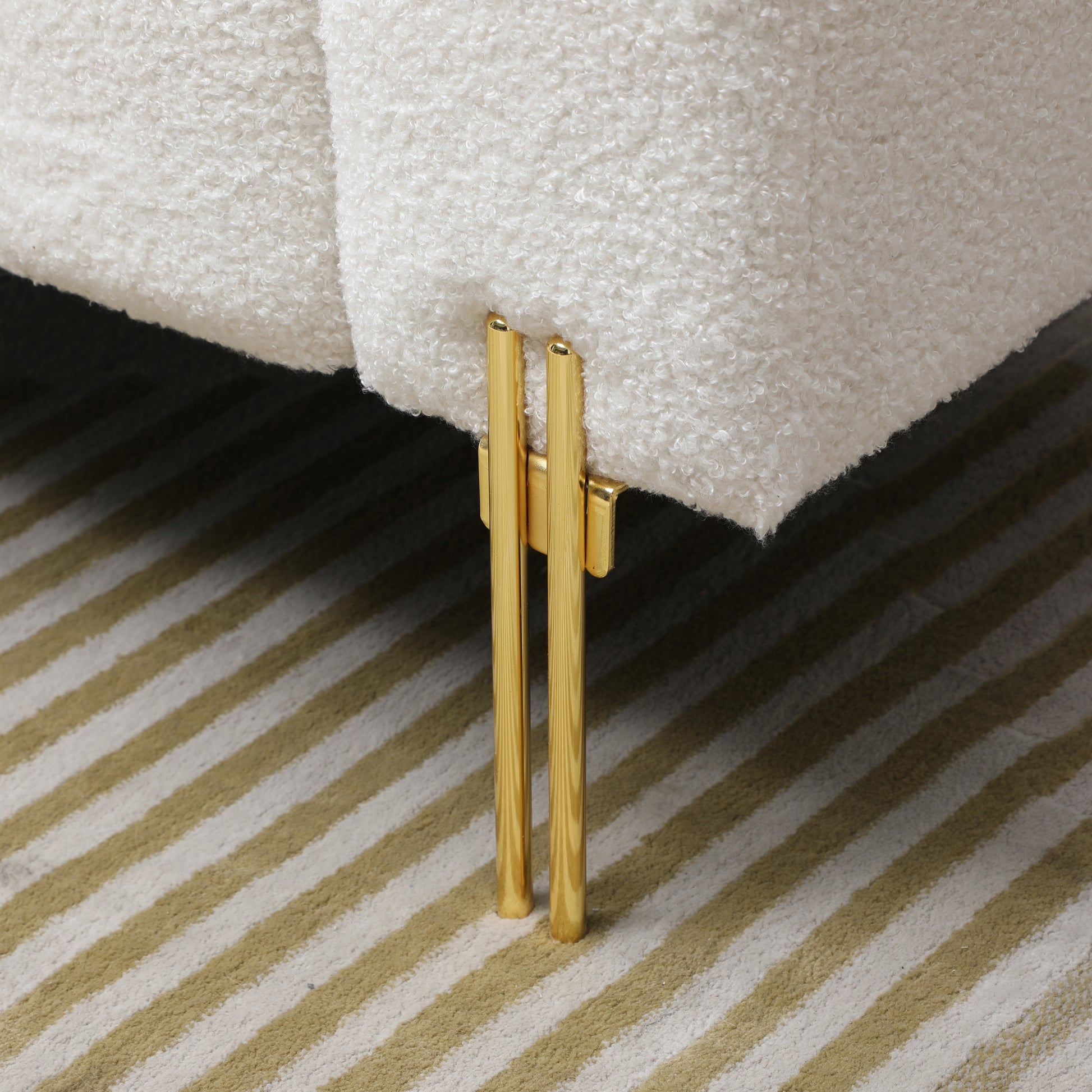 Closeup of plush white boucle fabric sofa leg with polished gold accents modern furniture