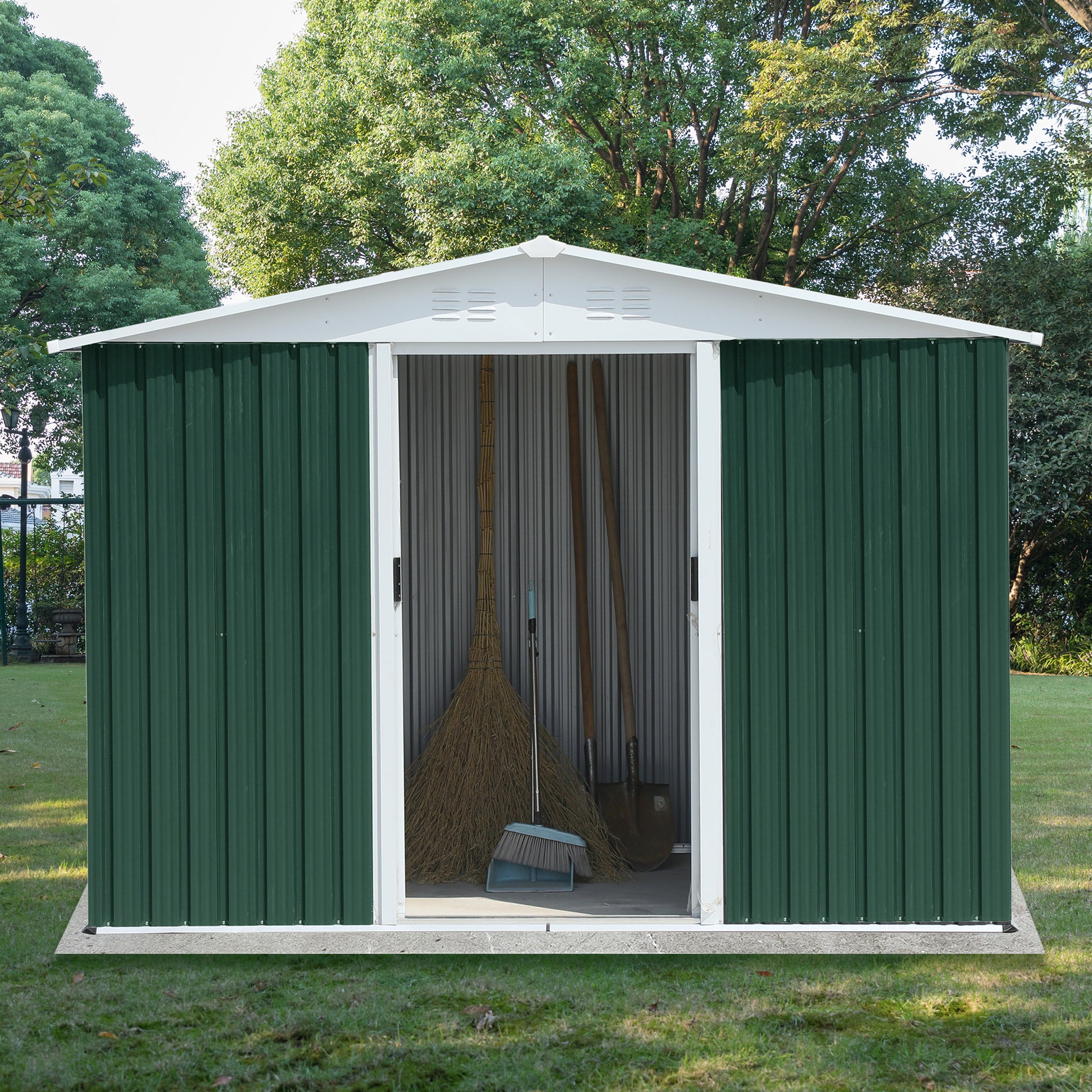 Green metal garden shed with white trim storing broom and shovel
