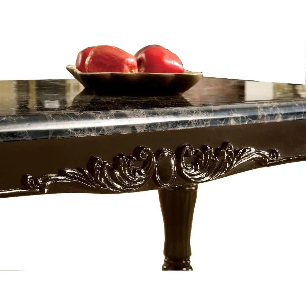 Closeup of a black marbletop dining table with ornate carved detailing and a decorative fruit bowl