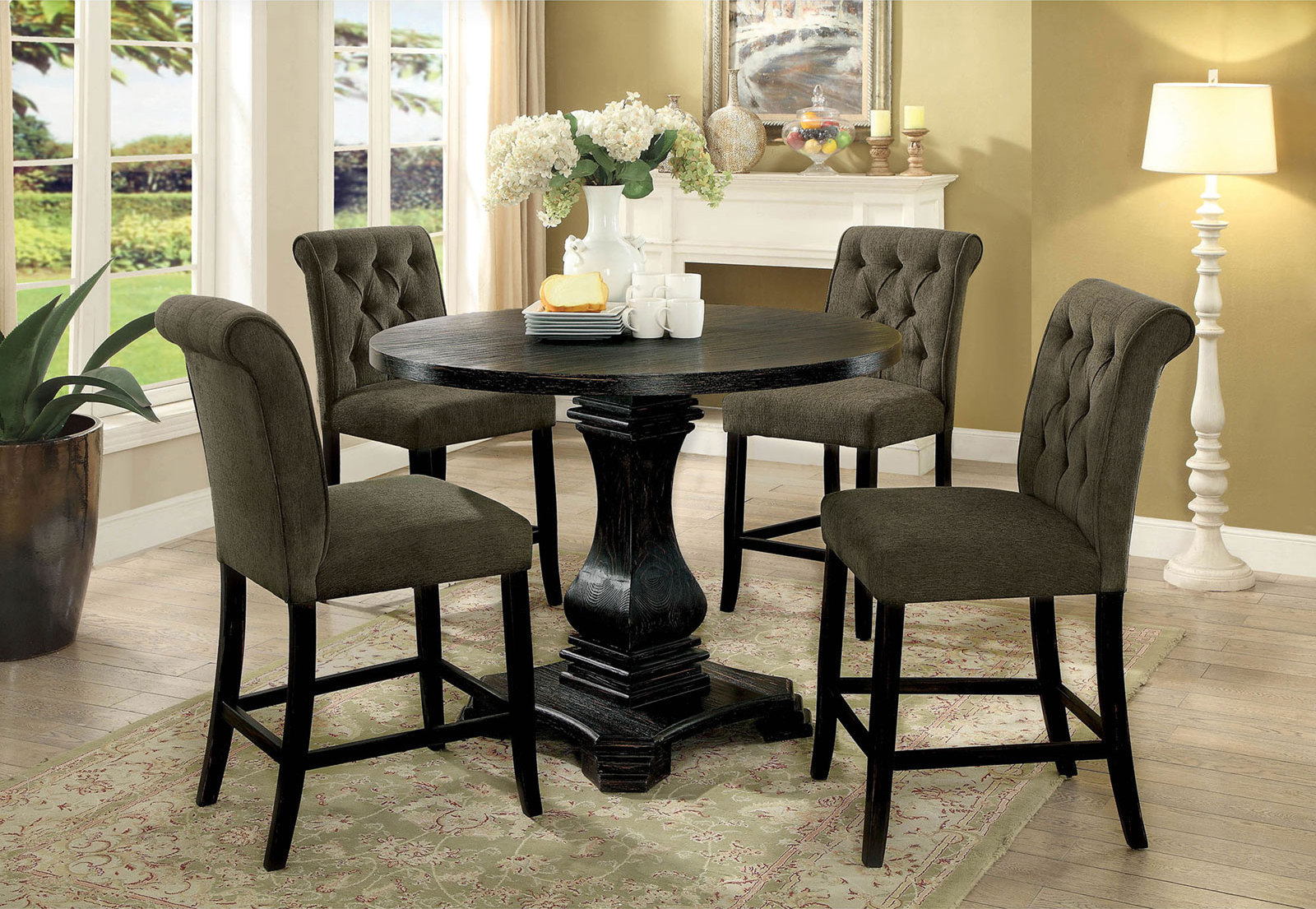 Dark wood pedestal dining table with four tufted grey counter chairs and a floral centerpiece