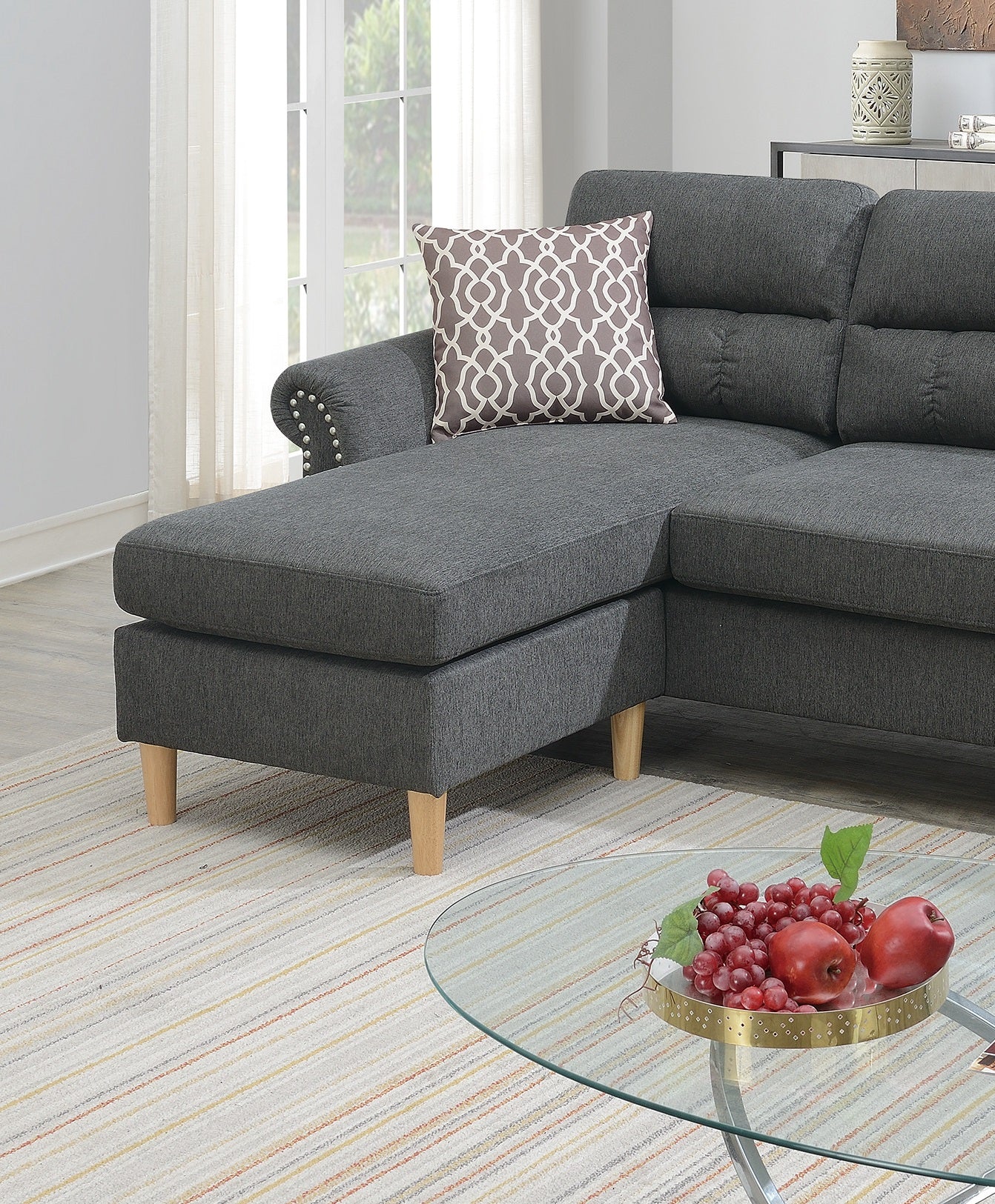 Dark grey fabric sectional sofa with decorative nailhead trim and a geometric throw pillow