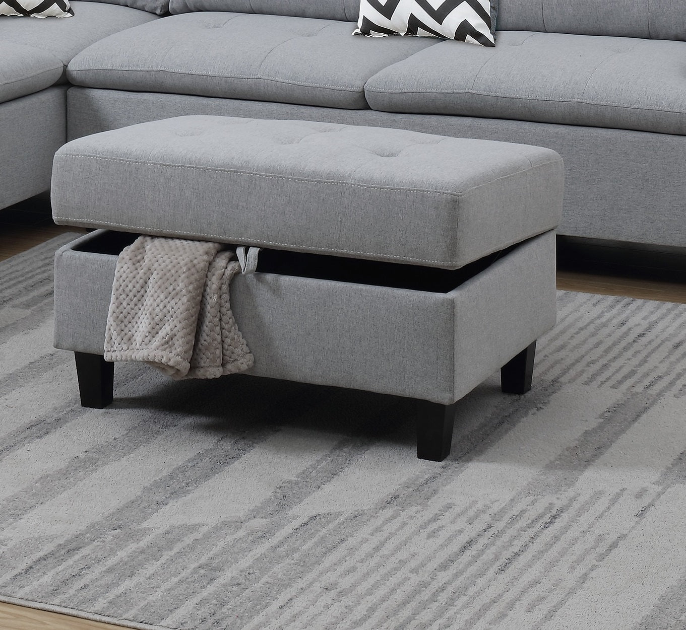 Grey upholstered storage ottoman with open lid revealing a blanket
