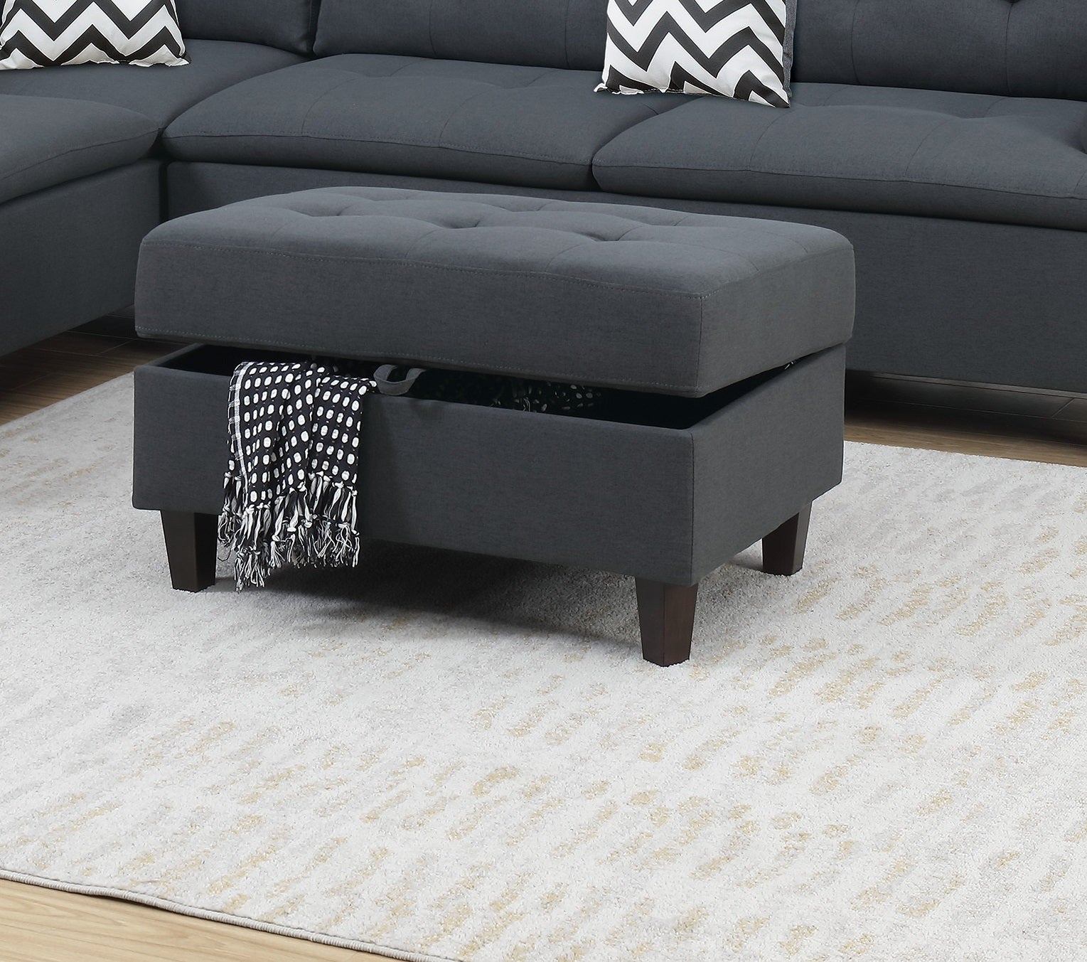 Dark gray upholstered storage ottoman with tufted lid open revealing blanket