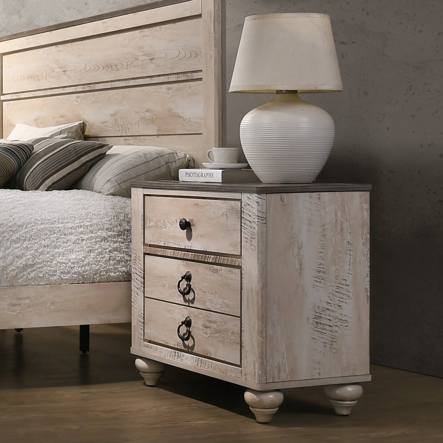 Distressed white wood nightstand with three drawers and antique brass ring pulls by a bed