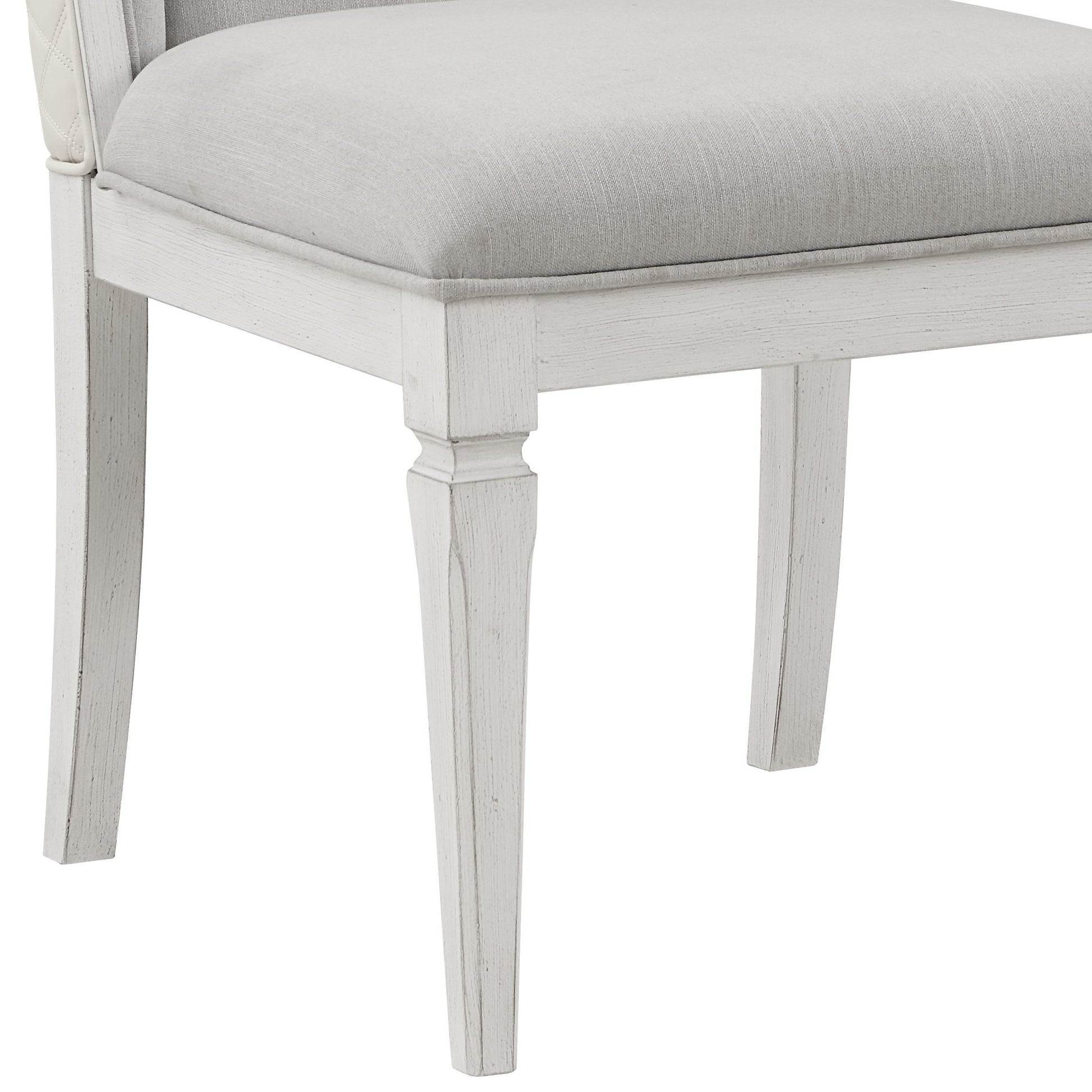 Closeup of a tufted white leather armchair armrest with a light grey linen seat cushion