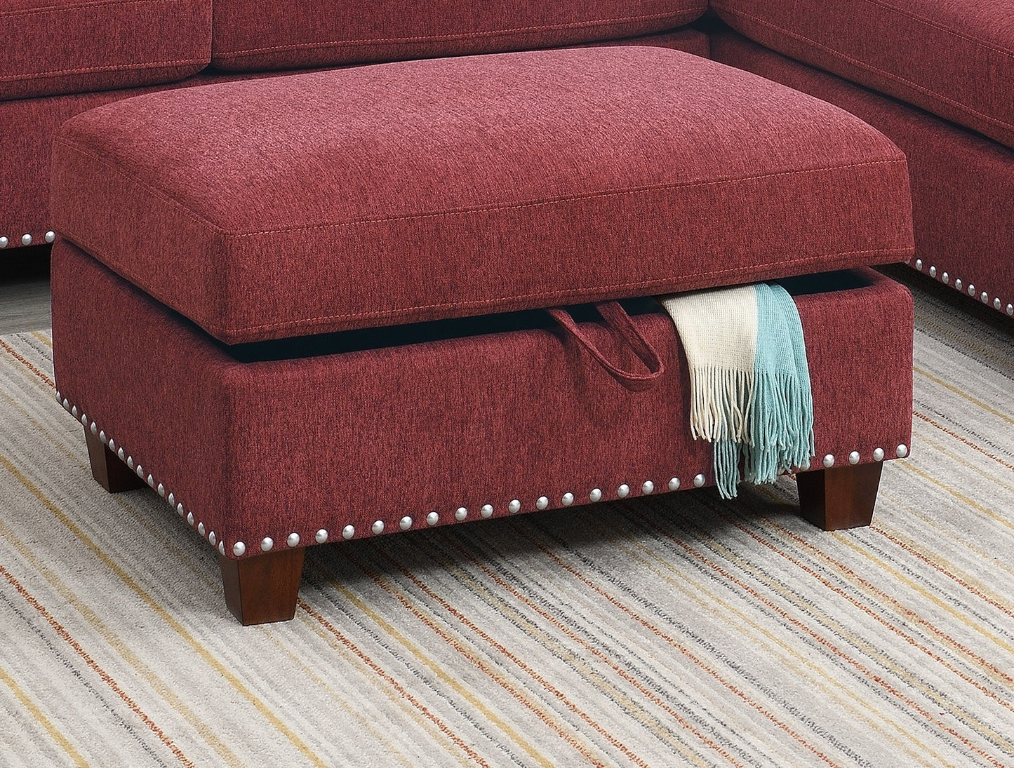 Red upholstered storage ottoman with silver nailhead trim and wooden legs