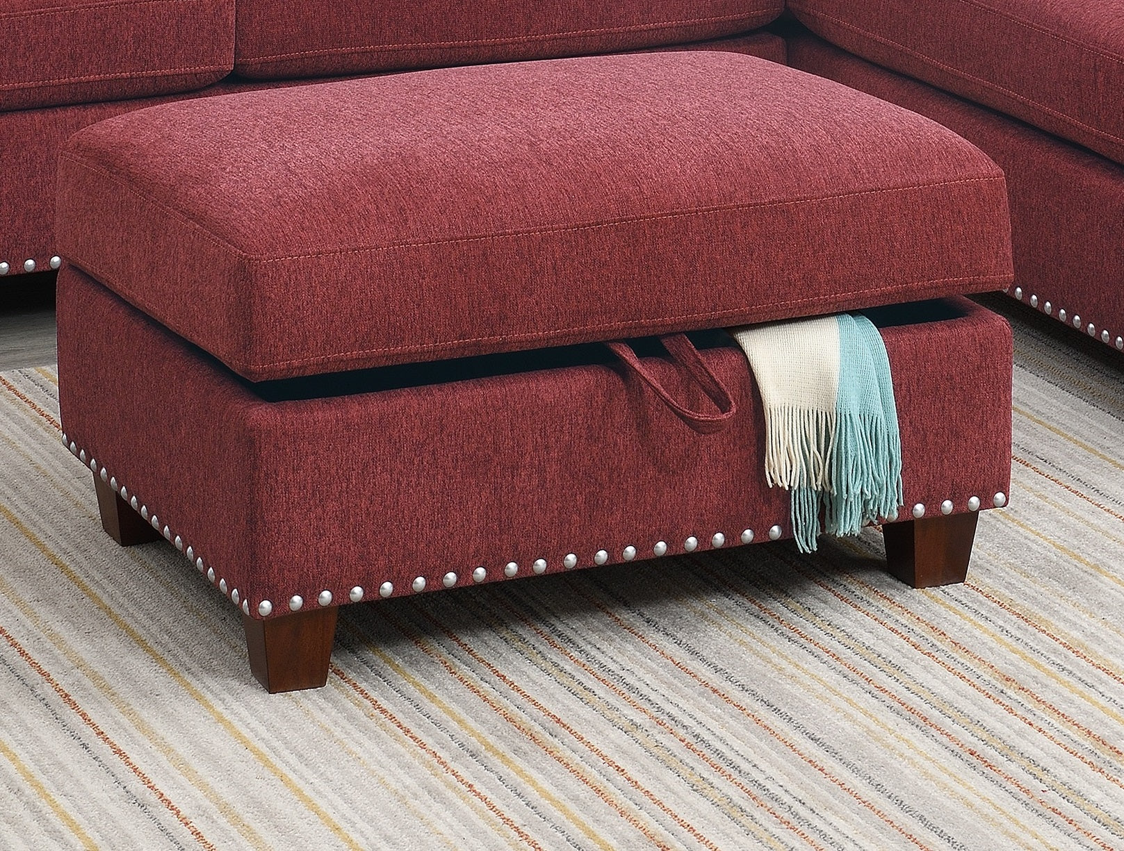 Red upholstered storage ottoman with silver nailhead trim and wooden legs