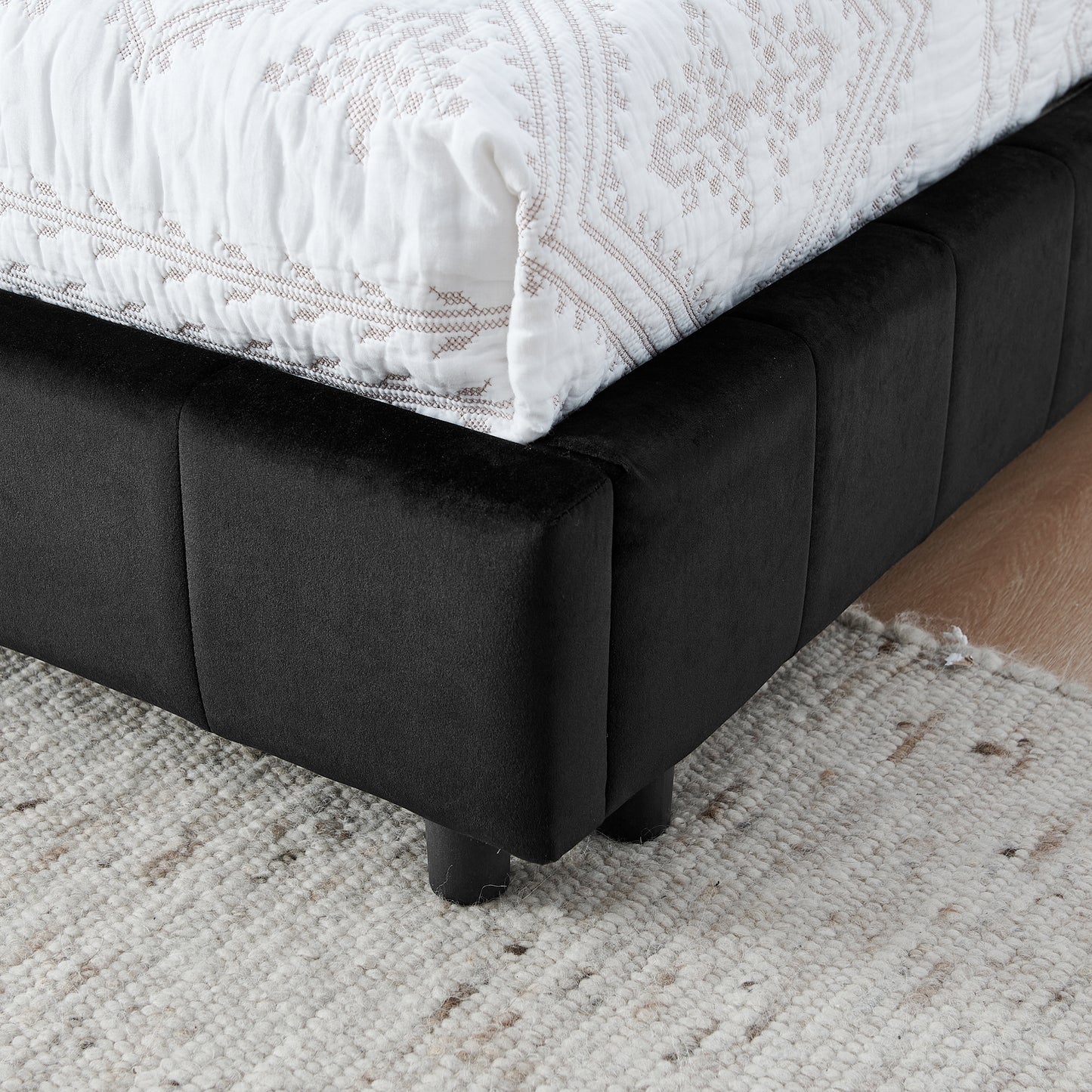 Closeup of a black velvet upholstered bed frame with decorative stitching on the white duvet cover