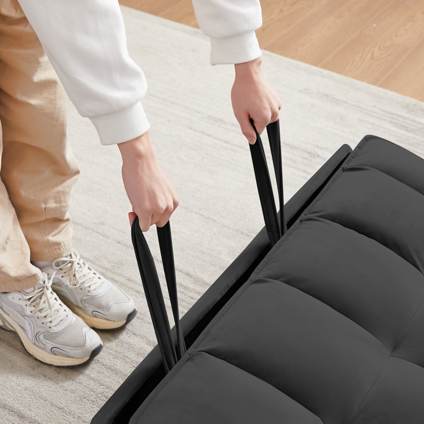 Persons hands pulling straps on a dark grey tufted futon sofa bed