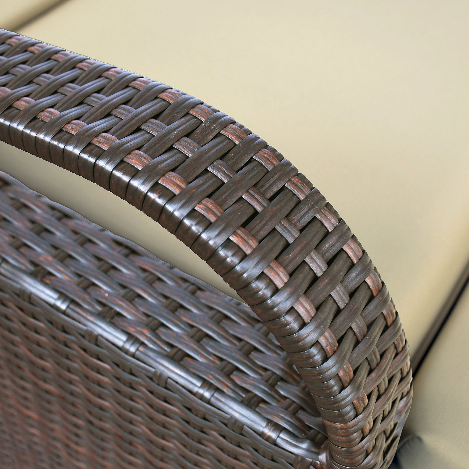 Closeup of dark brown wicker weave on a patio chair armrest with beige cushion