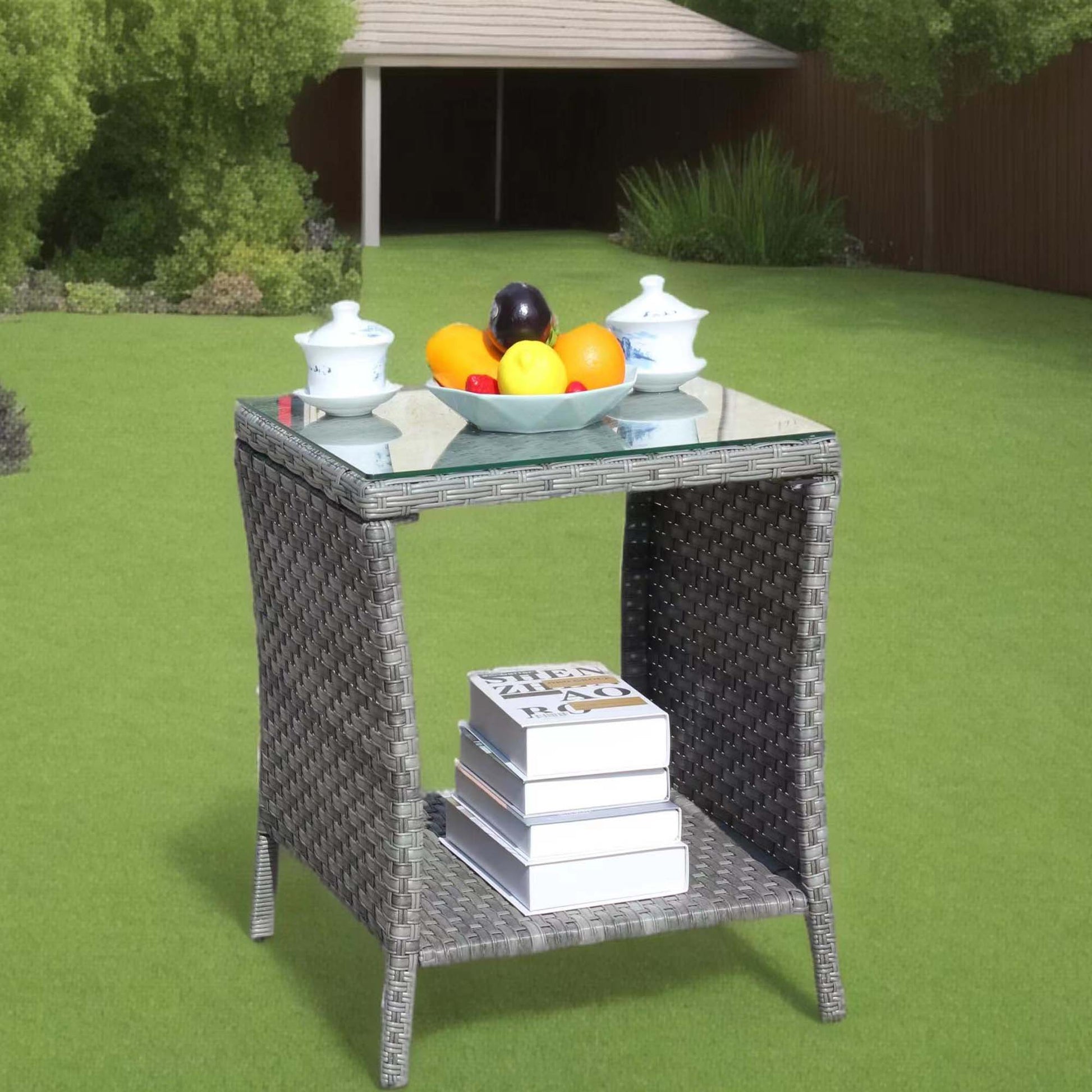 Gray wicker patio side table with glass top featuring fruit bowl and books