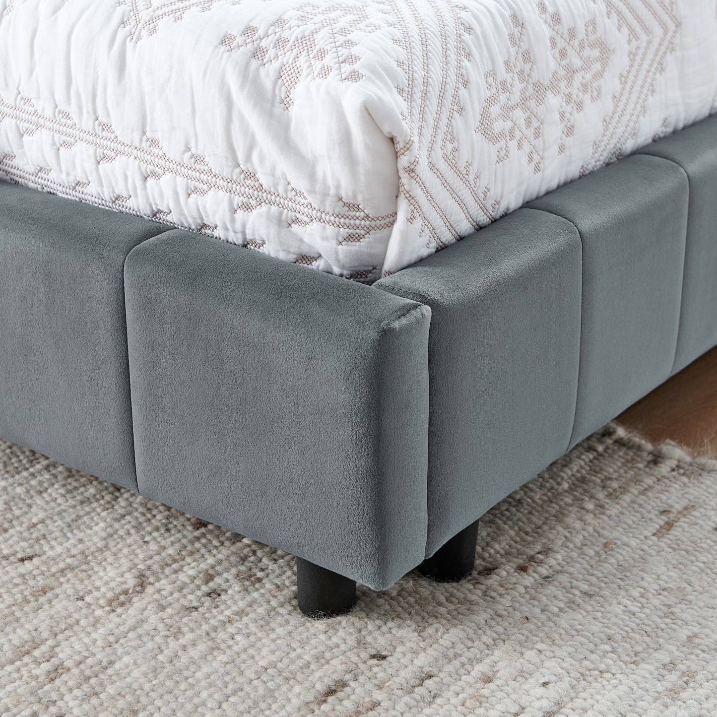 Modern grey velvet upholstered bed frame with a quilted white comforter and tufted headboard