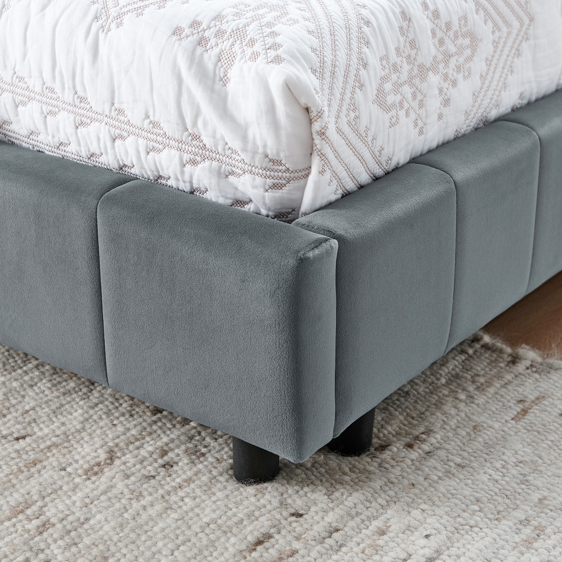 Modern grey velvet upholstered bed frame with a quilted white comforter and tufted headboard