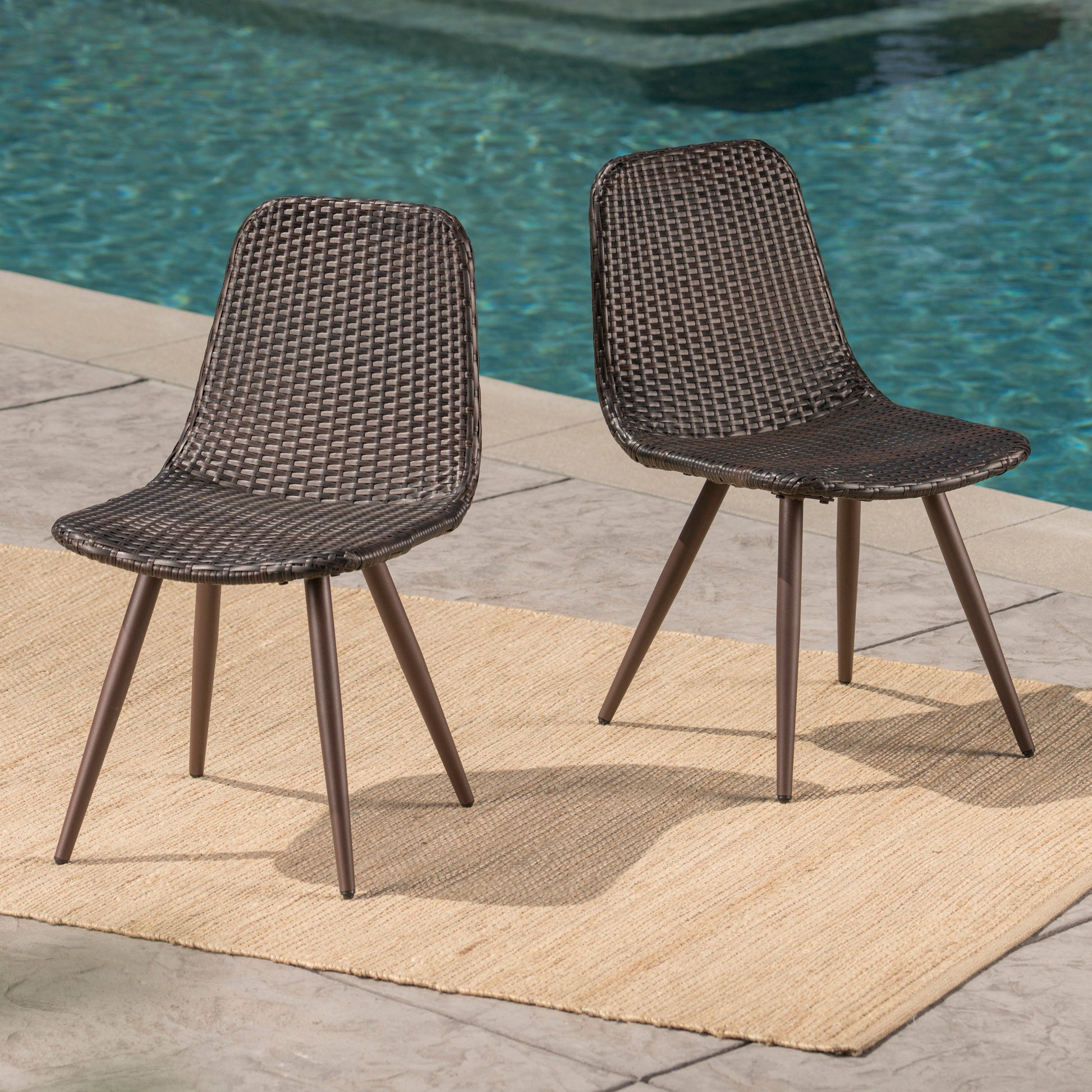 Two dark brown wicker outdoor chairs with metal legs on a beige rug near a pool