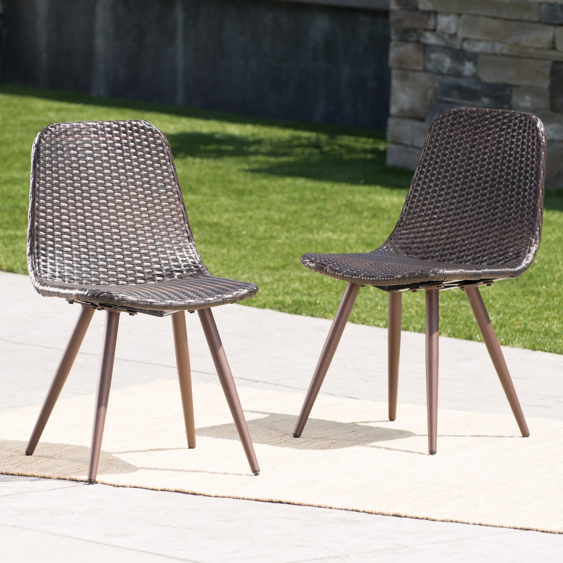 Pair of brown woven resin patio chairs with bronze legs on outdoor rug