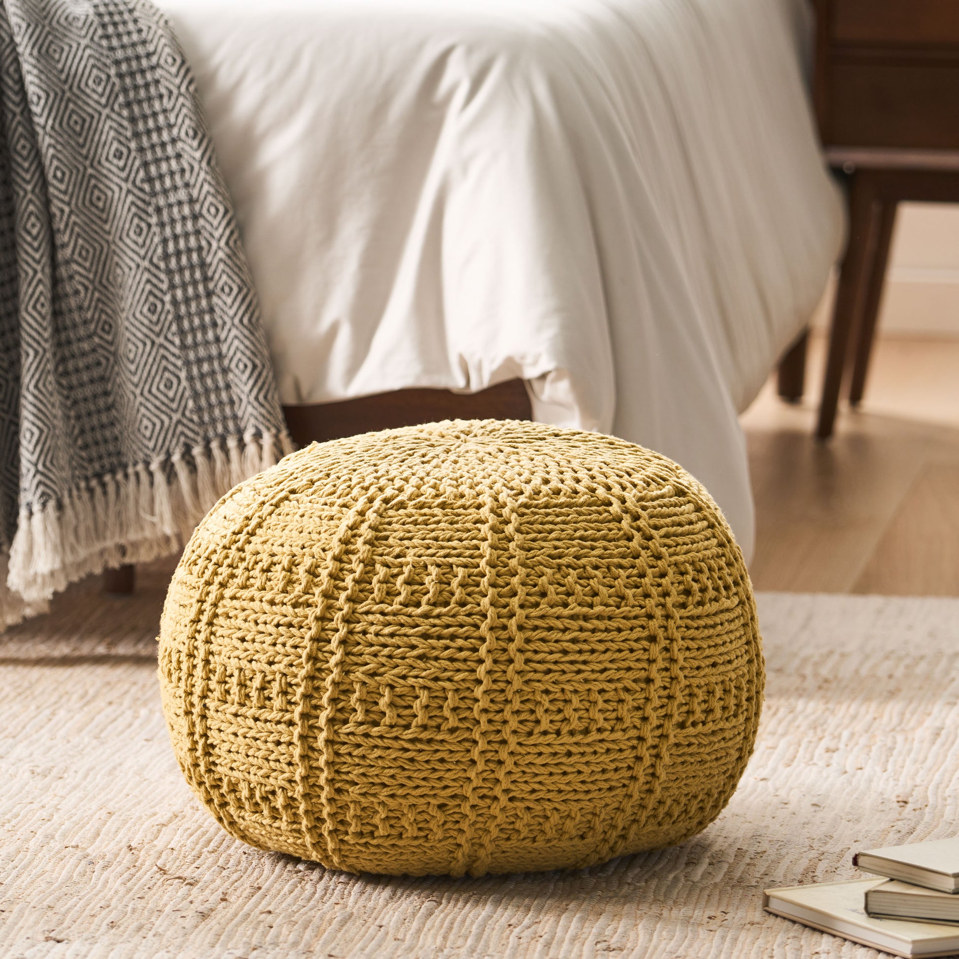 Mustard yellow knitted pouf with intricate stitch pattern on woven rug