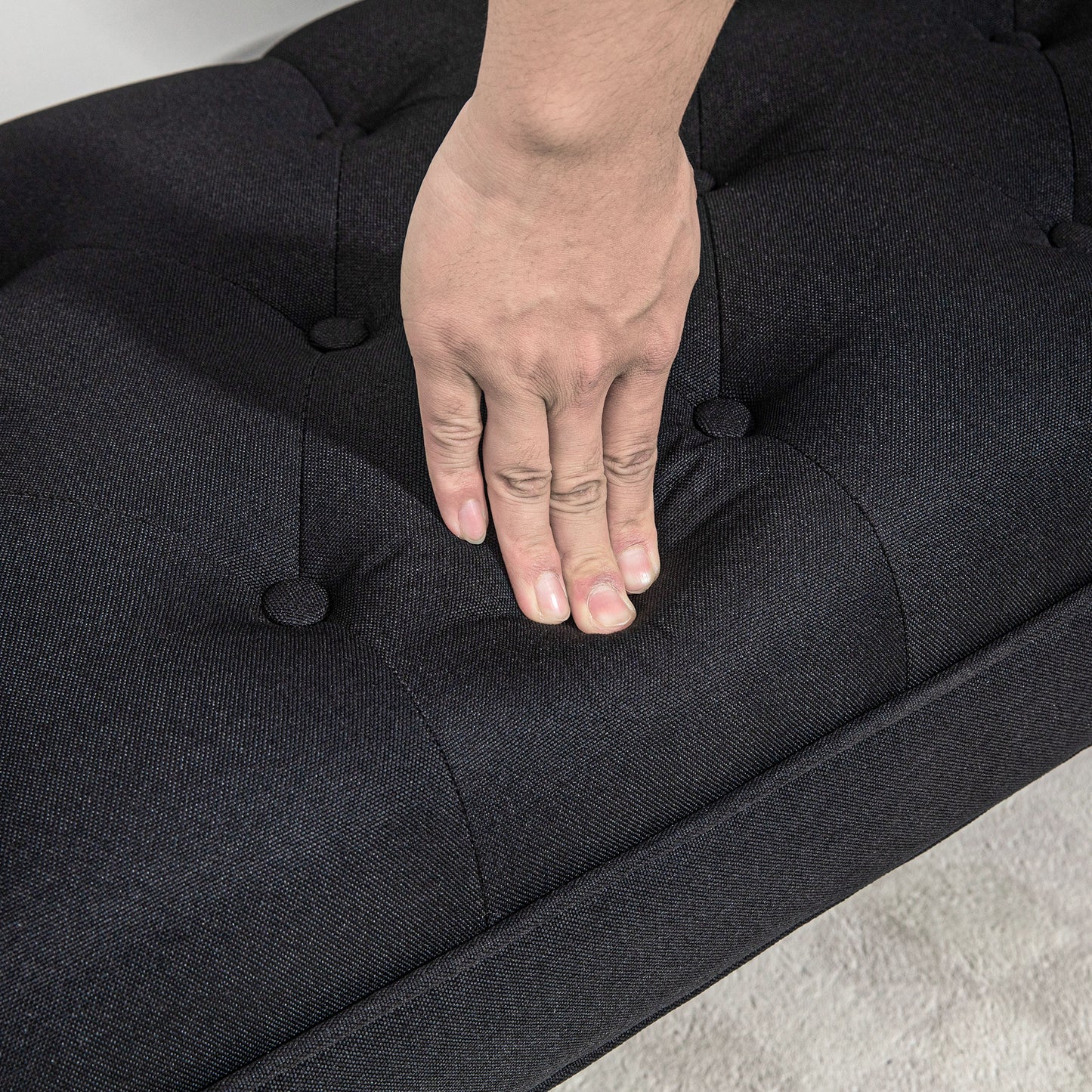 Black upholstered bench seat with tufted buttons and a hand pressing down