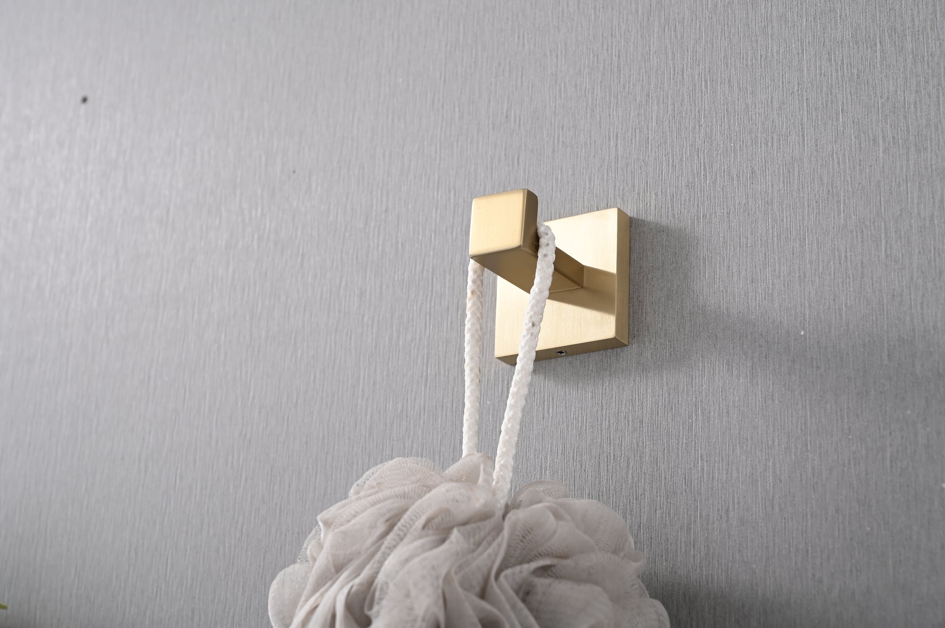 Brushed brass wall hook holding a white loofah perfect for a modern bathroom