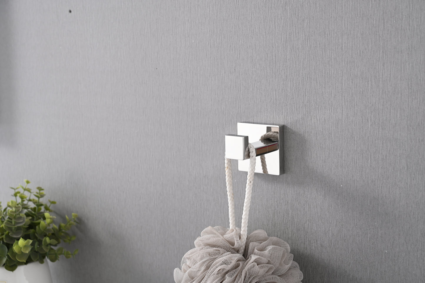 Polished chrome square robe hook mounted on textured gray wall holding a white bath pouf