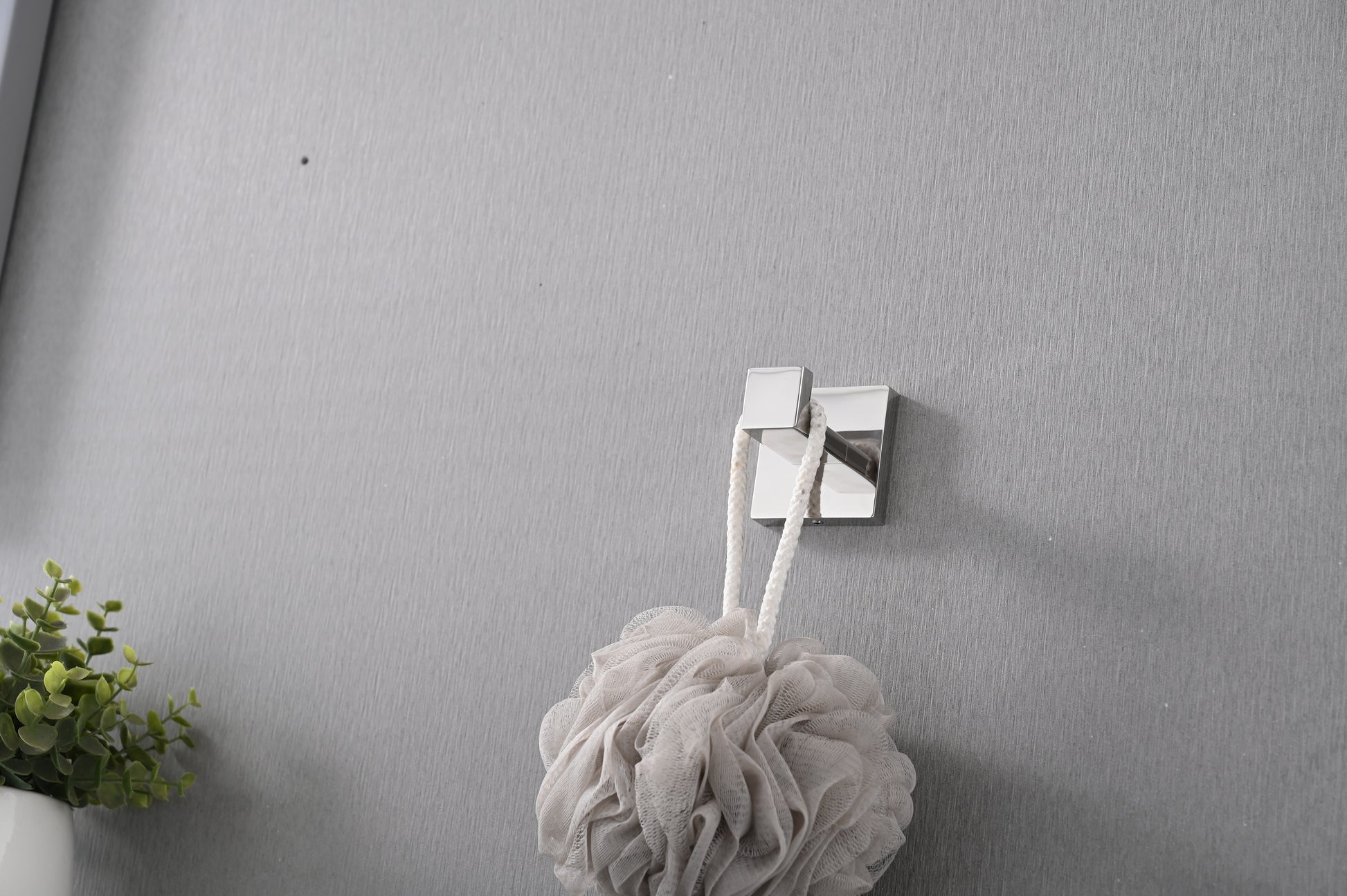 Creamy mesh bath pouf with rope hanging on a silver square hook