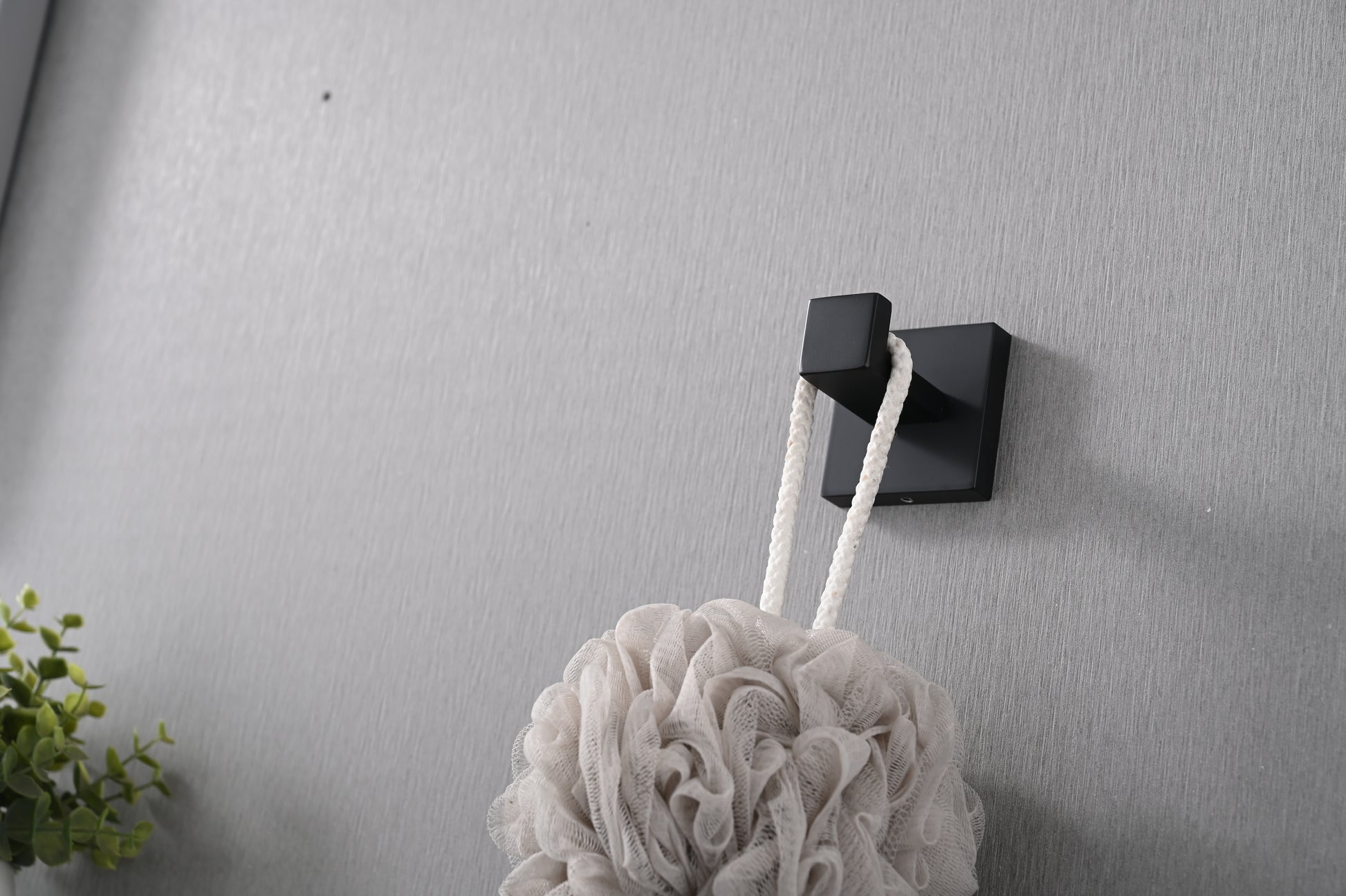 Black modern wall hook holding a light beige bath pouf