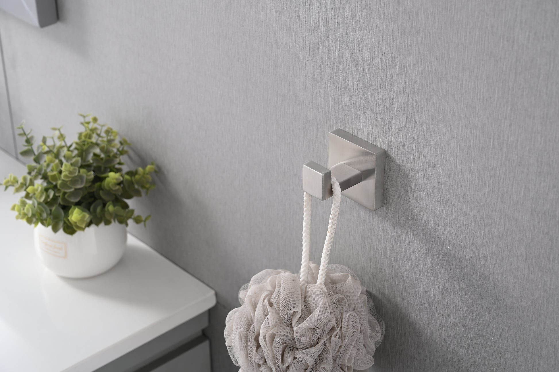Brushed nickel wall hook with a square base holding a white mesh shower pouf