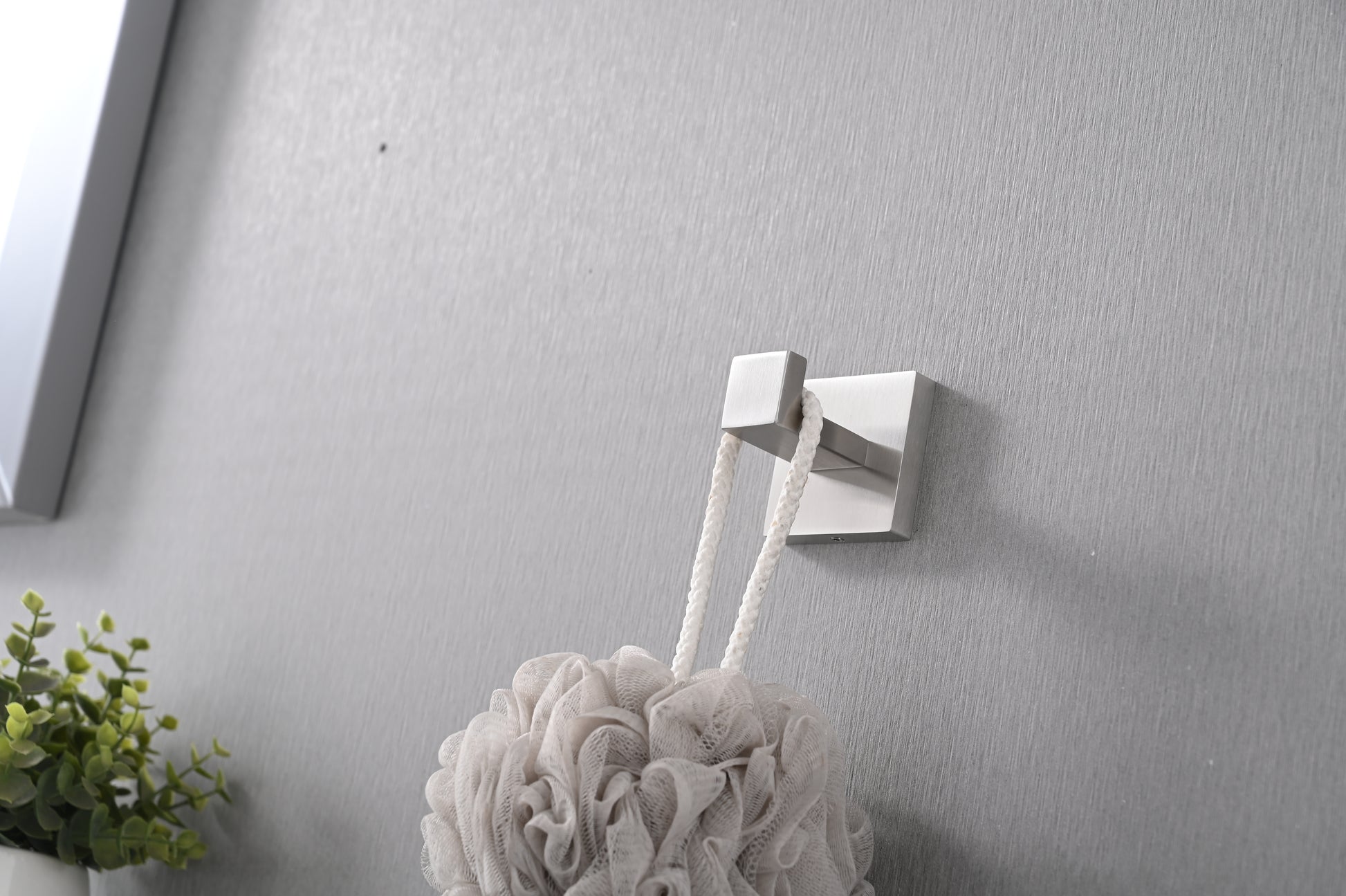 Brushed nickel wall hook holding a white bath pouf with thick rope hanger