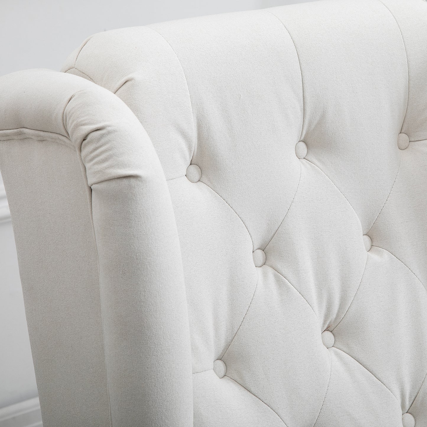 Closeup of a cream linen armchair with tufted back and rolled armrest detail
