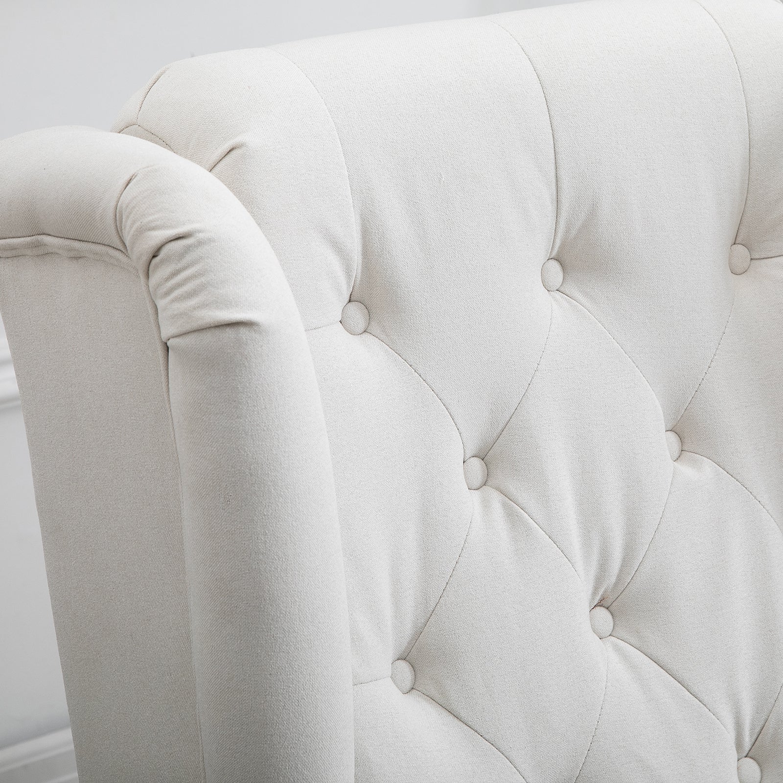 Closeup of a cream linen armchair with tufted back and rolled armrest detail
