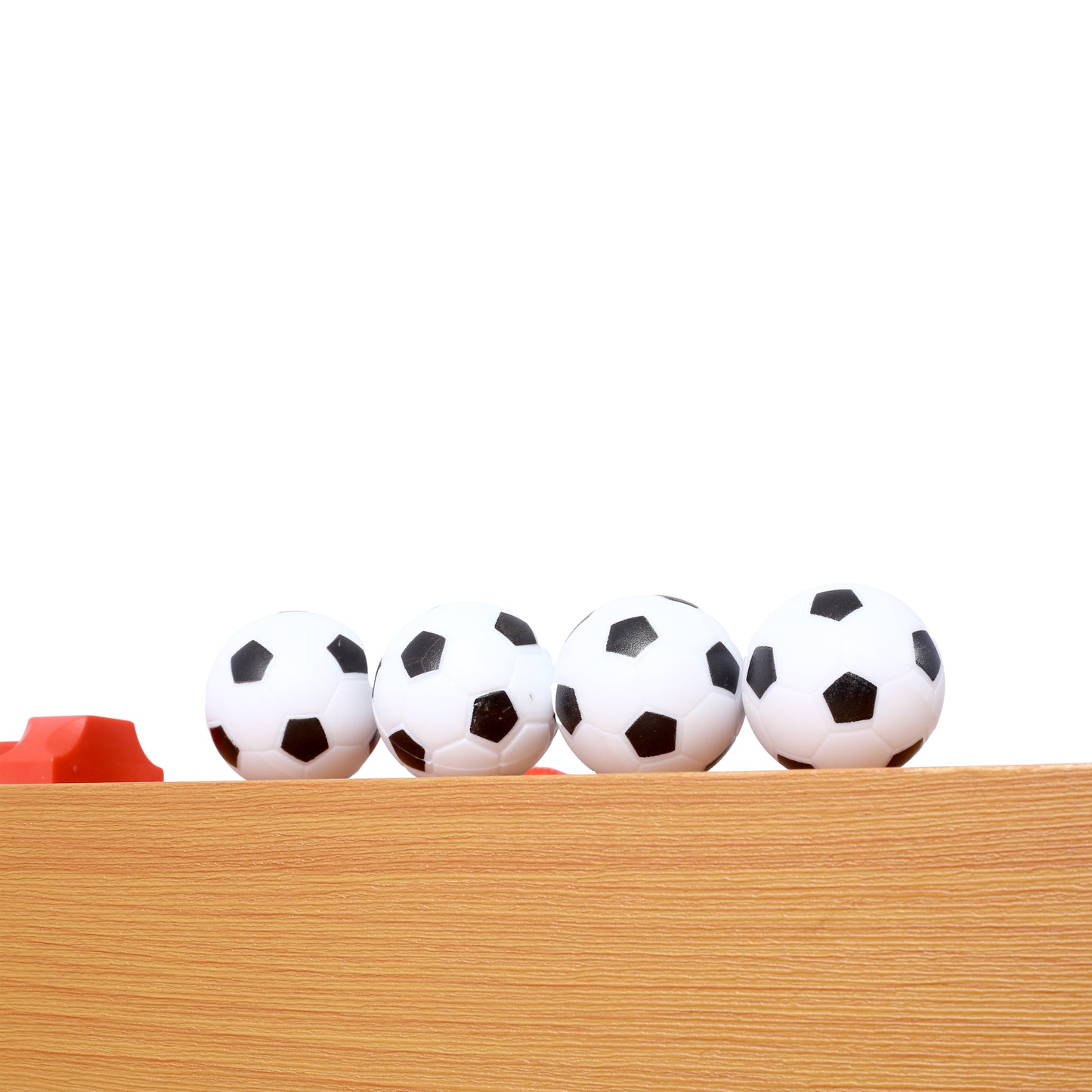 Four mini soccer balls in black and white on a wooden surface with a red obstacle