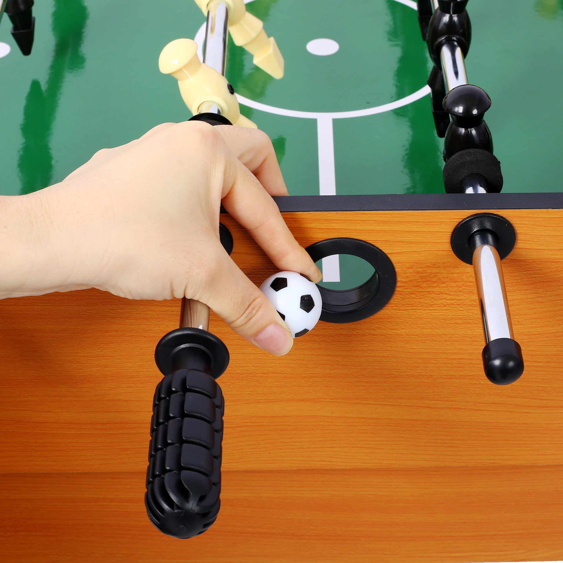 Hand placing a mini soccer ball on a tabletop foosball game with green turf