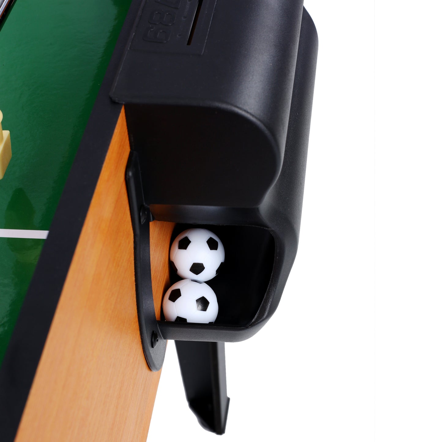 Two miniature soccer balls with black pentagons stored in a black compartment of a tabletop soccer game