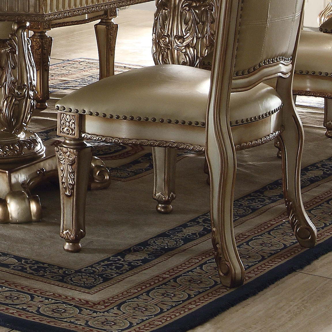 Elegant cream upholstered dining chair with ornate gold detailing and nailhead trim