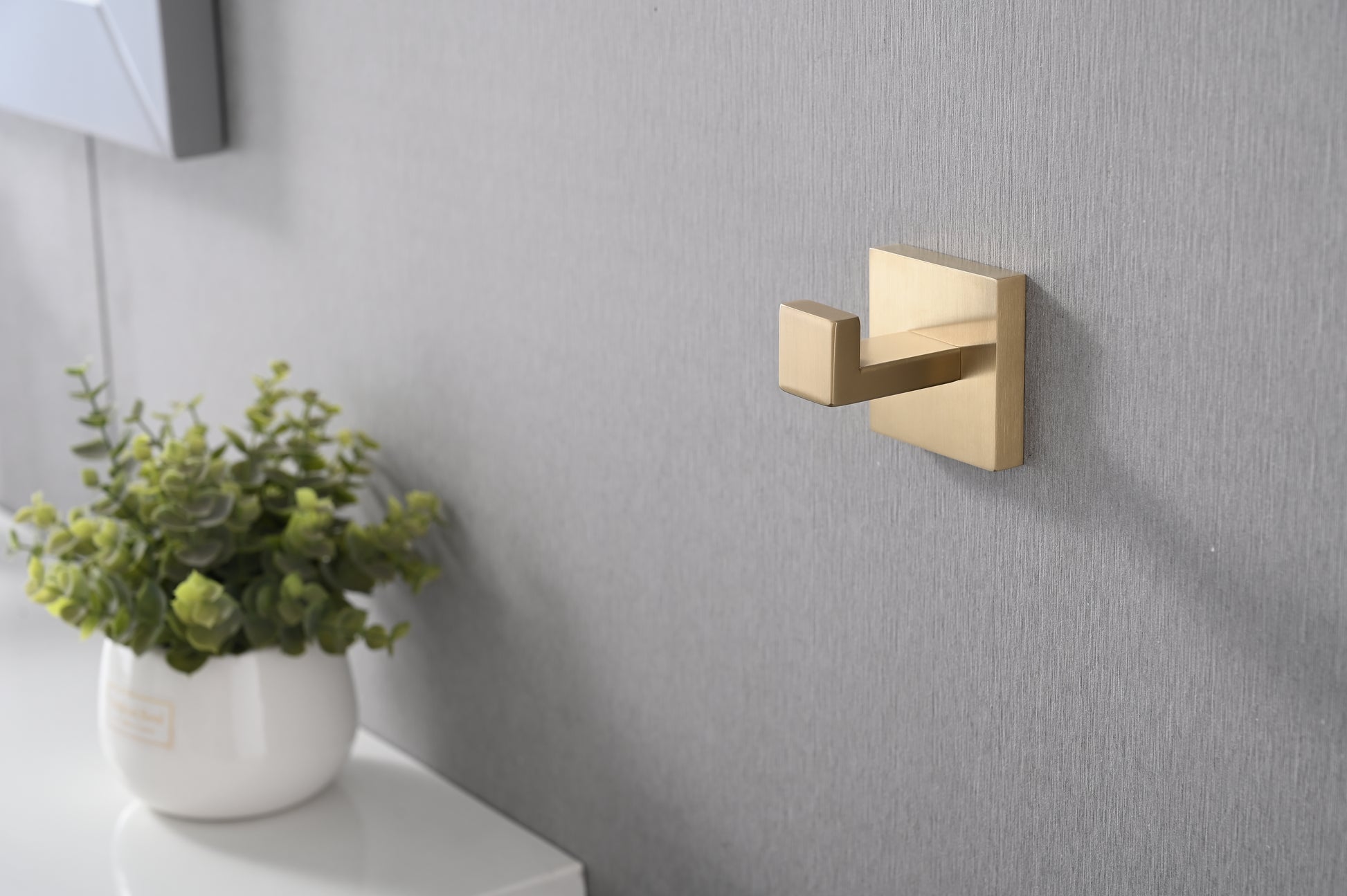 Brushed brass modern hook mounted on a textured grey wall  characters