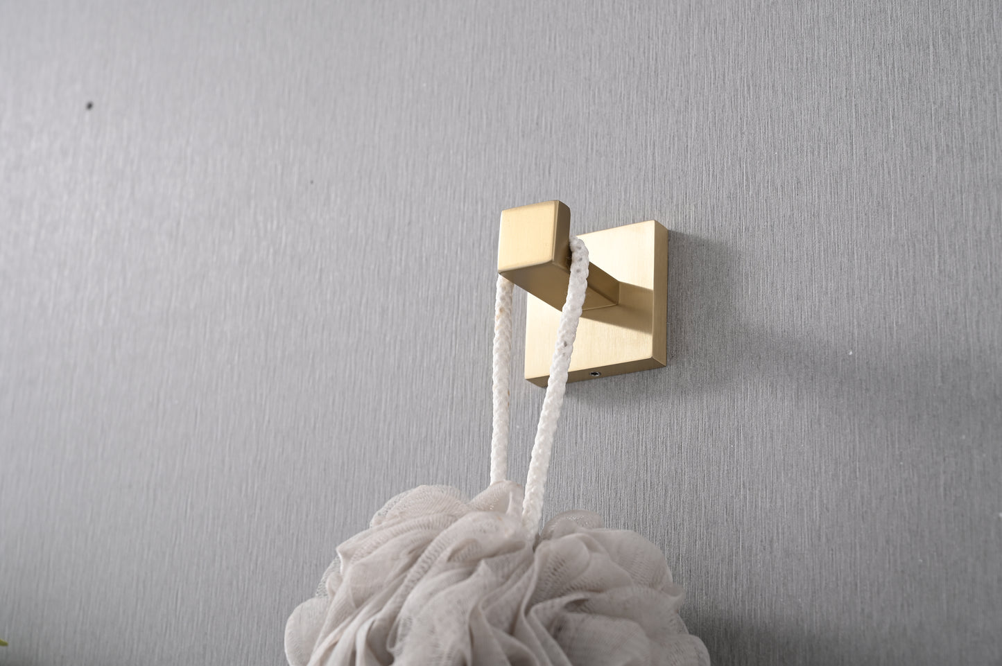 Brushed brass wall hook with a minimalist square base holding a white pouf