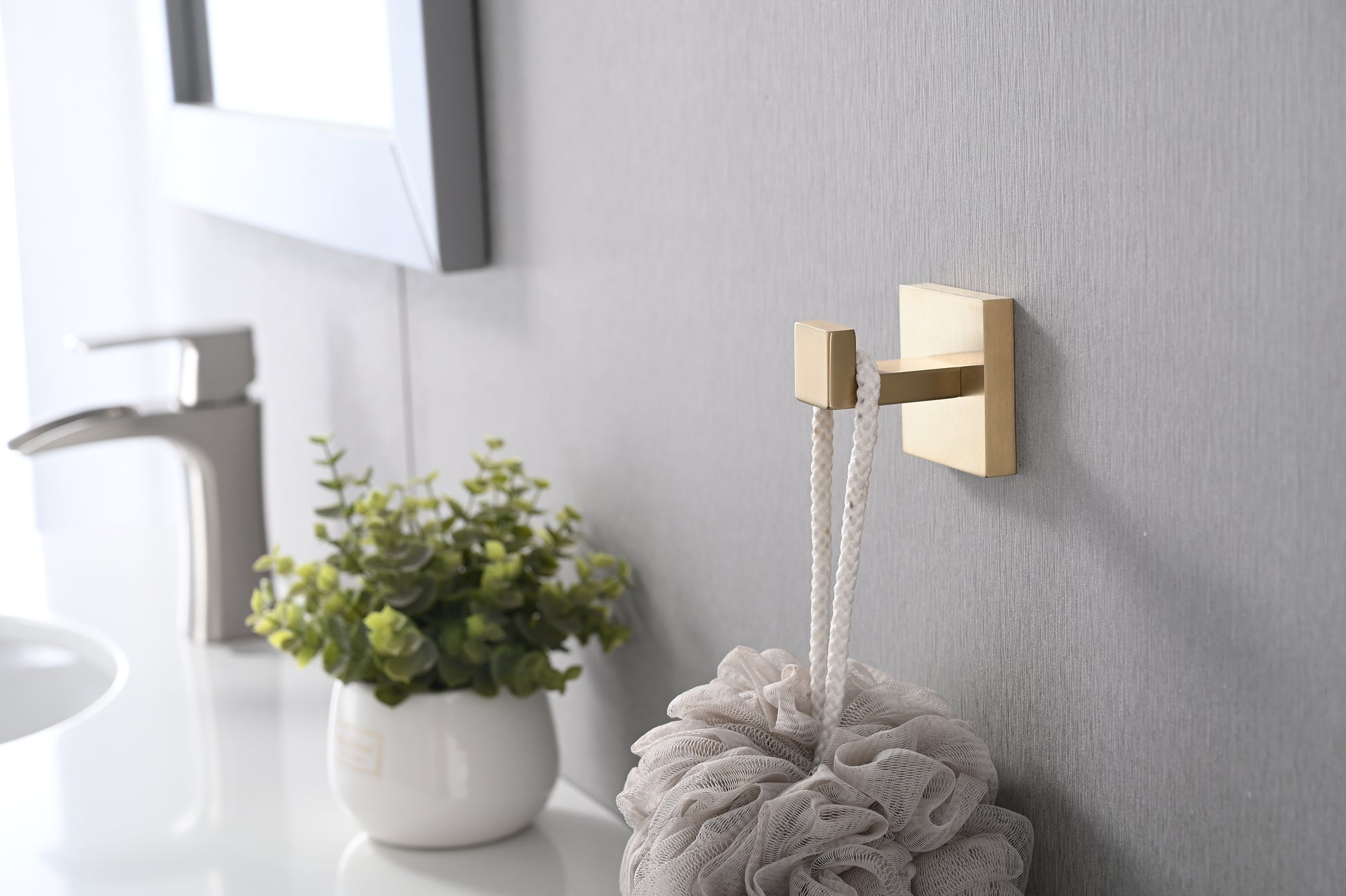 Modern brushed gold wall hook holding a white bath pouf
