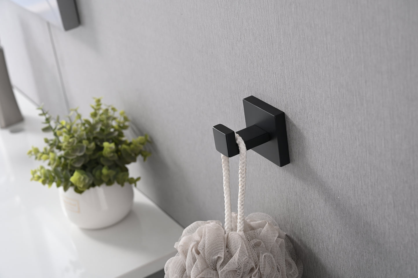 Modern black wall hook with square base and single arm holding a white mesh bath pouf