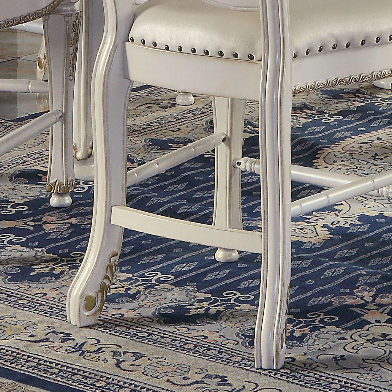 White ornate dining chair legs with gold accents on a patterned rug