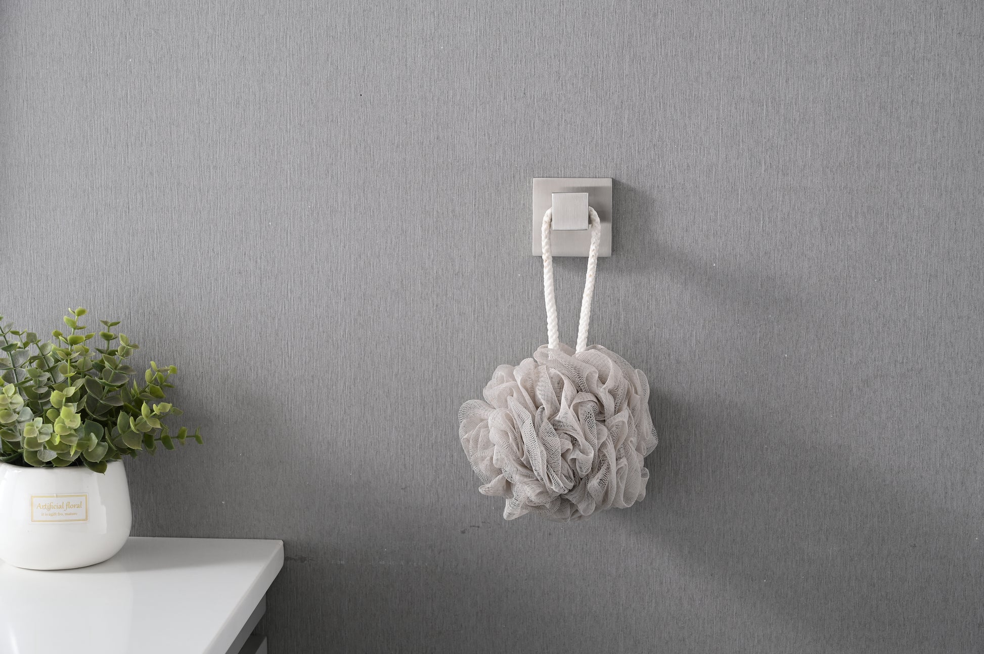 Soft grey mesh bath pouf with white rope hanger on wall hook