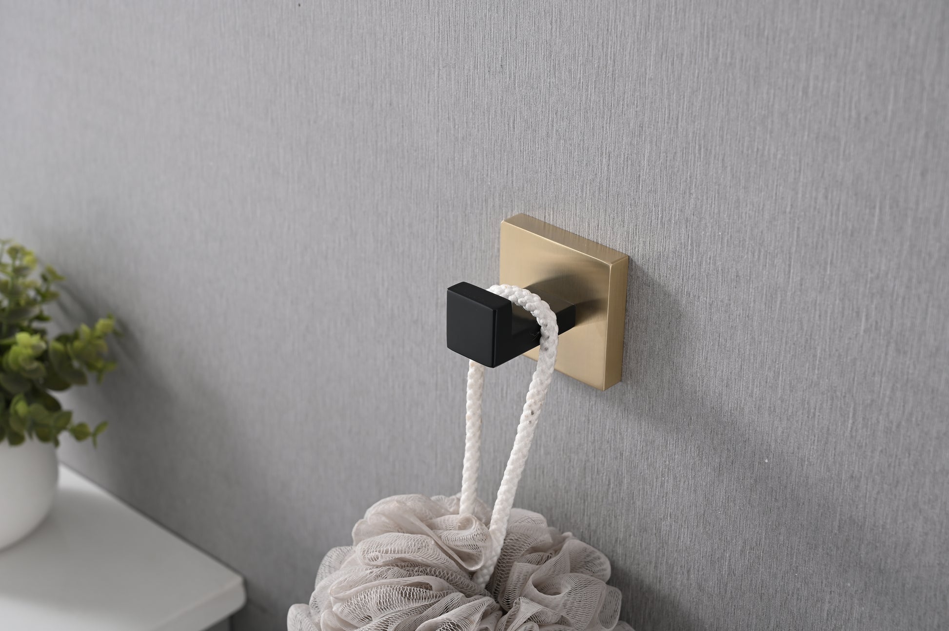 Brushed brass and black modern bathroom hook holding a beige bath pouf