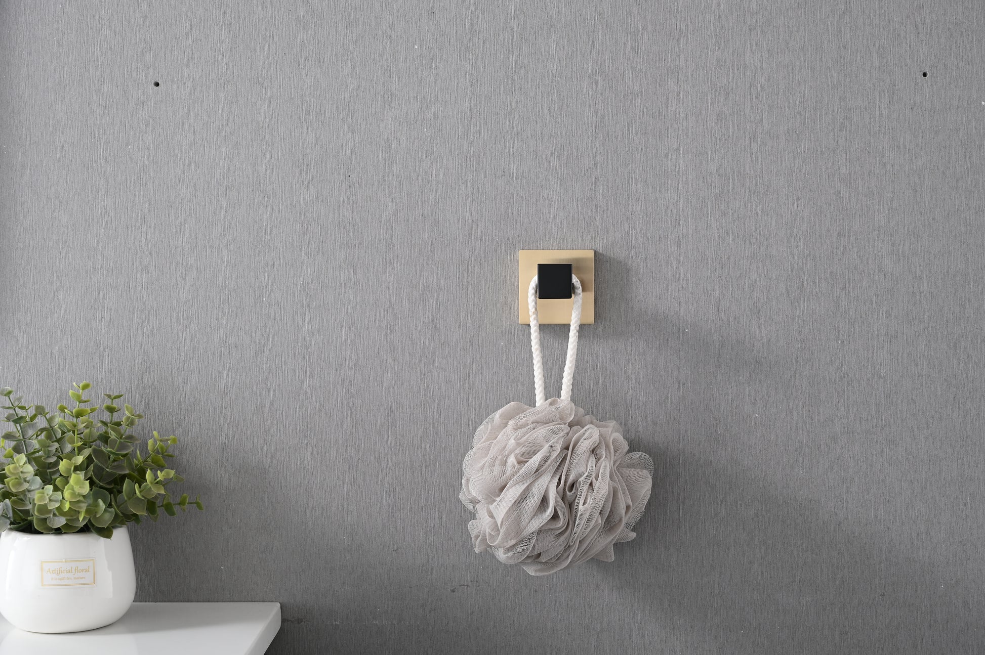 Textured grey loofah with a white rope hanging from a modern gold and black wall hook
